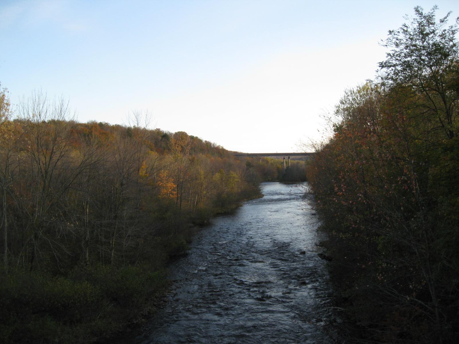 A river flows through a valley lined with autumn trees under a clear sky.