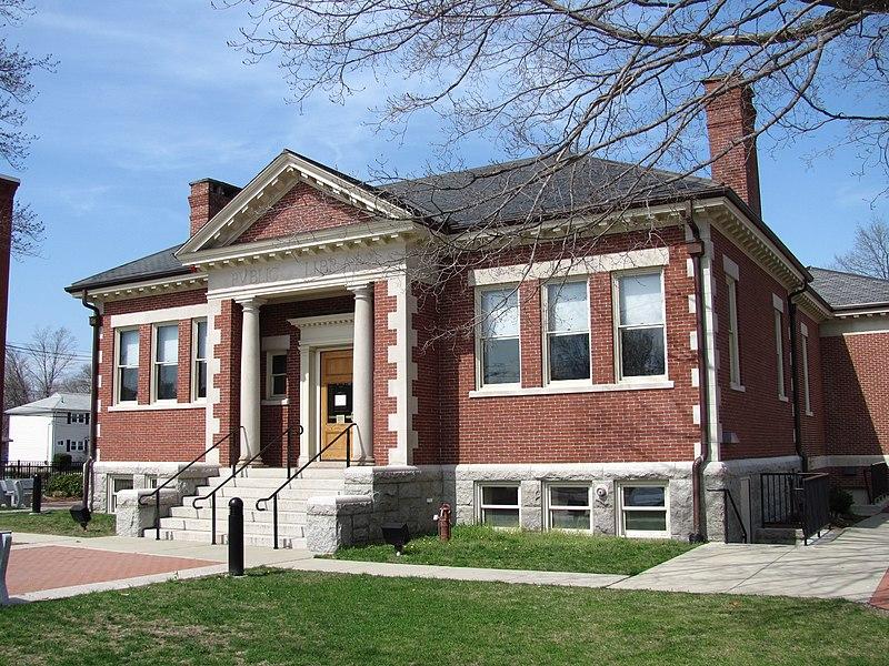 A red brick building with white columns and a grassy lawn on a sunny day.