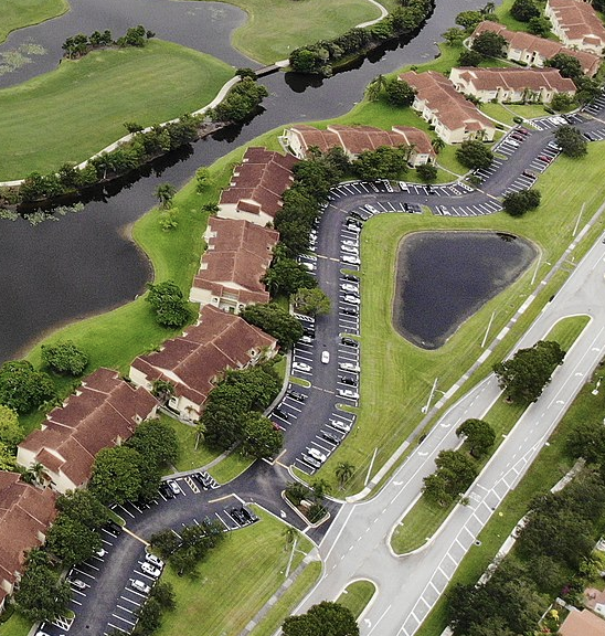 Aerial view of residential buildings, parking lots, roads, and water features.