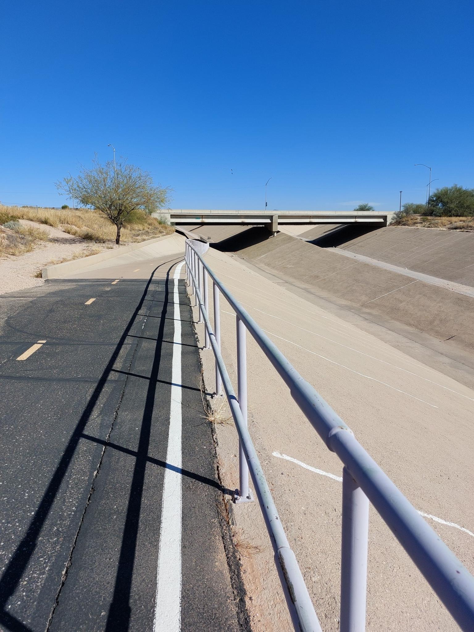Paved path with a metal railing leading to an overpass under clear sky.