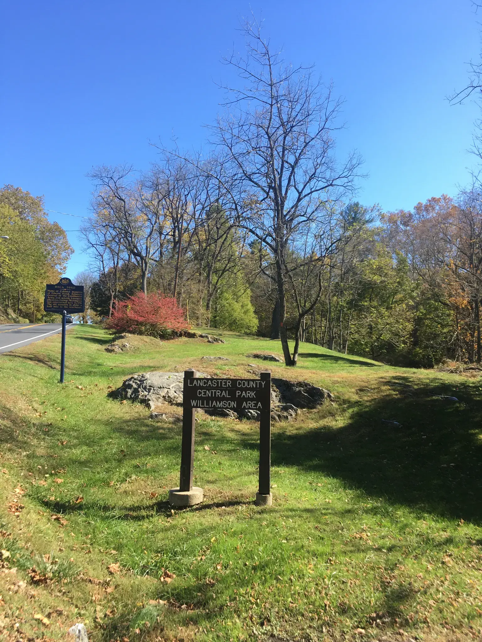 A wooden sign stands on a grassy hill with trees under a clear sky.