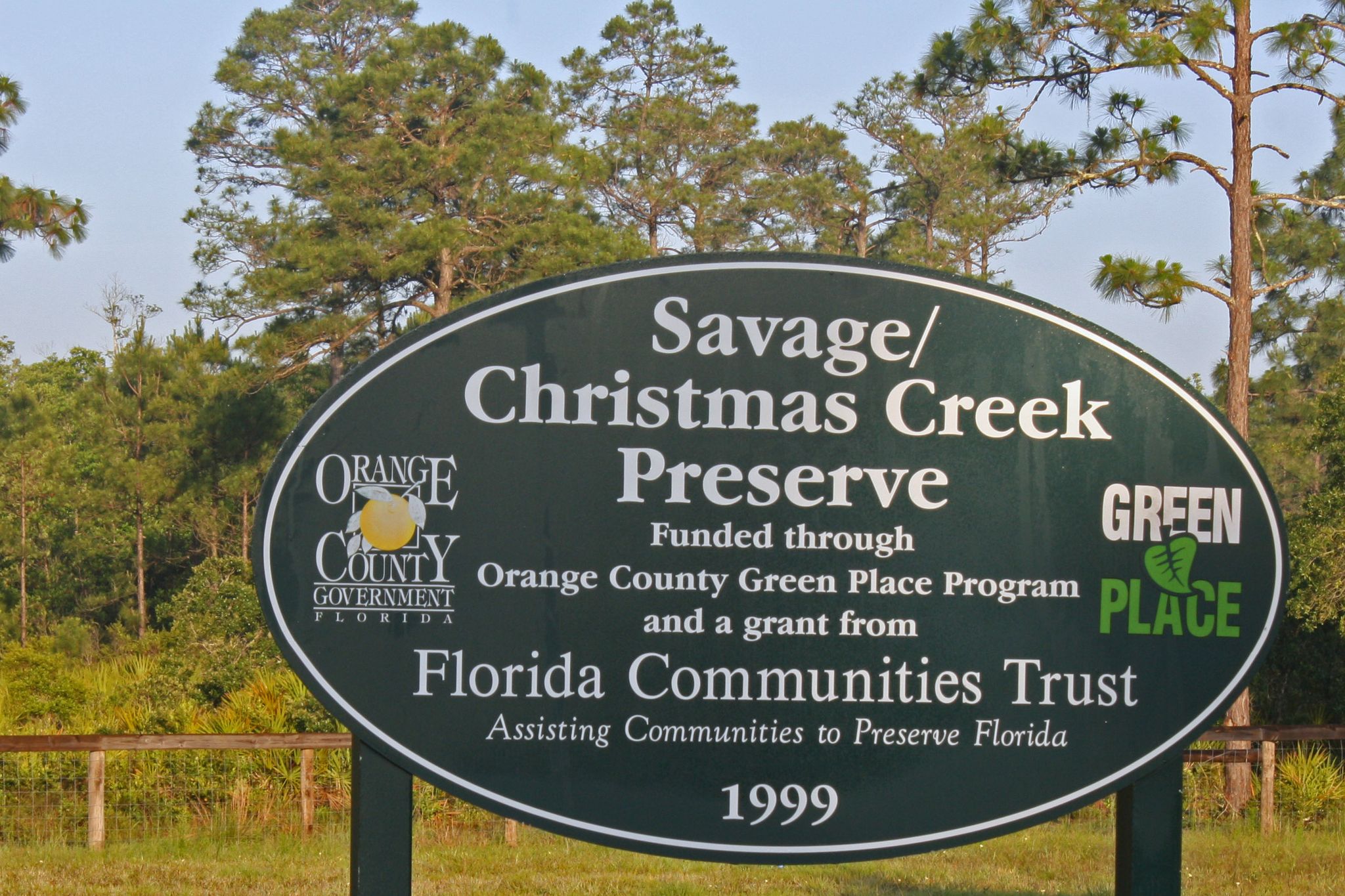 A large oval green sign stands in a grassy area with tall pine trees. - Savage/Christmas Creek Preserve from Titusville via Buck Lake Conservation Area loop