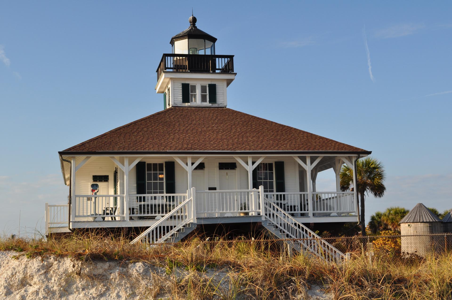 White house with a lighthouse tower on a grassy dune, sunny day.