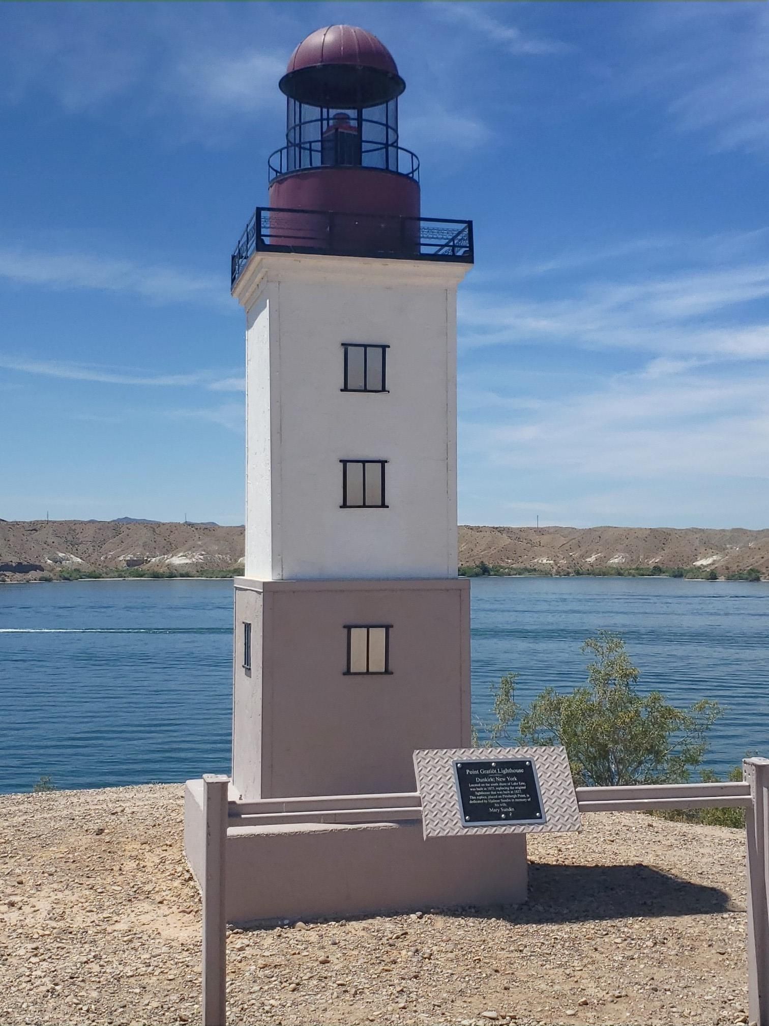 A white and red lighthouse stands by calm water under a clear blue sky. - Lake Havasu City loop