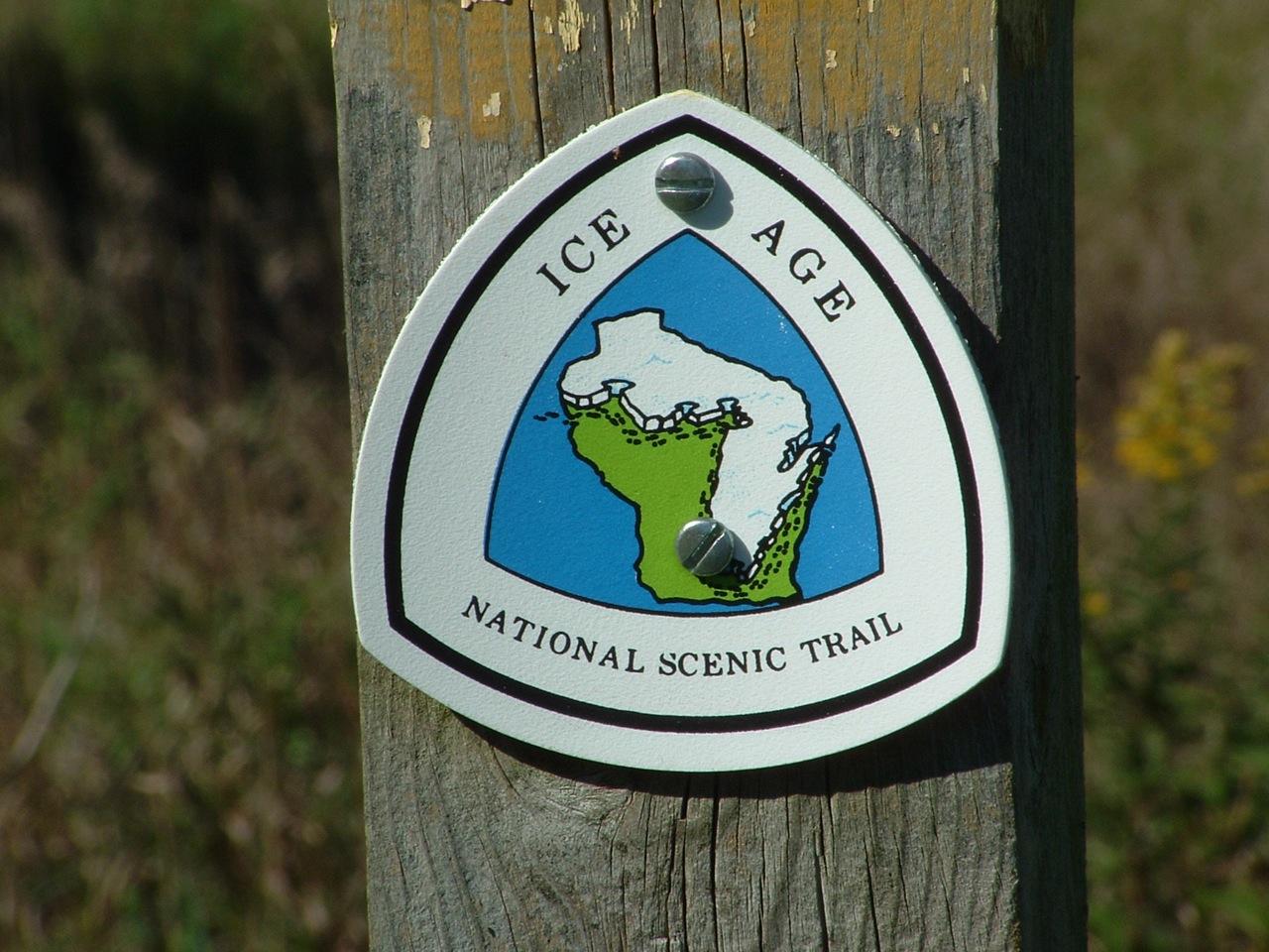 A white triangular trail marker with a map design on a wooden post.