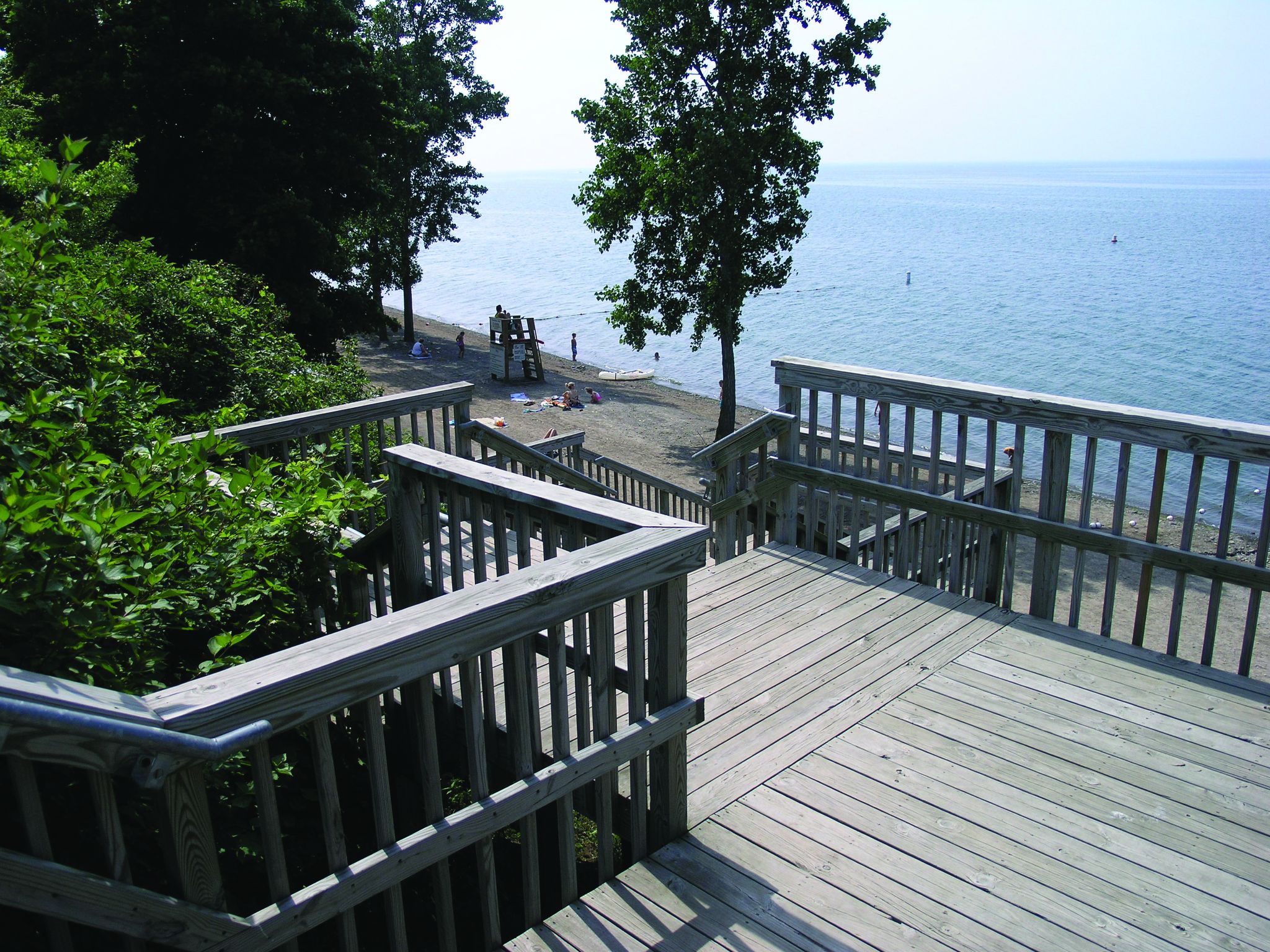 Wooden stairs and boardwalk lead down to a sunny beach with people. - Interpretive Trail