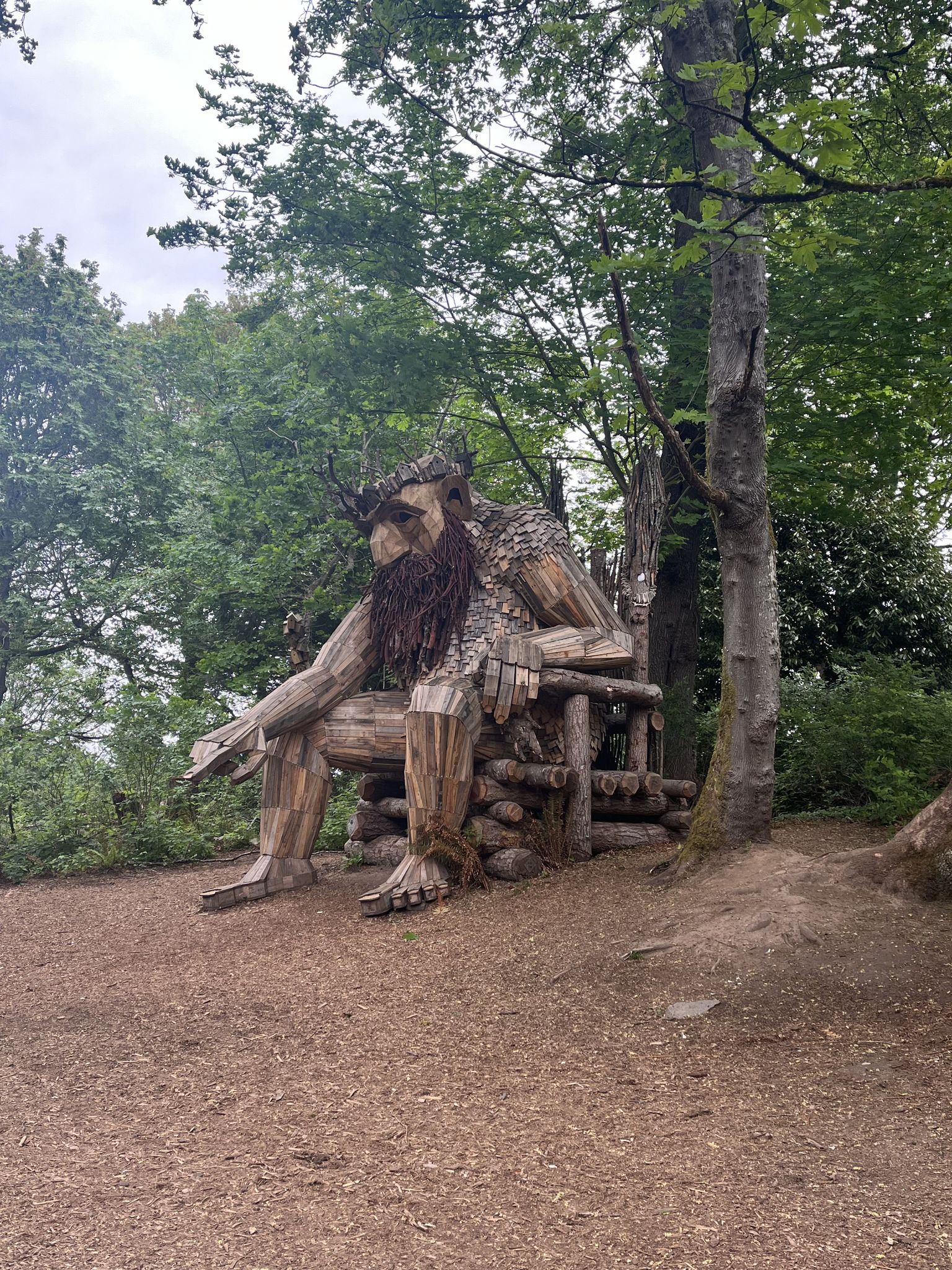 Large wooden sculpture of a bearded figure sitting in a forest clearing. - Point Robinson Park Loop