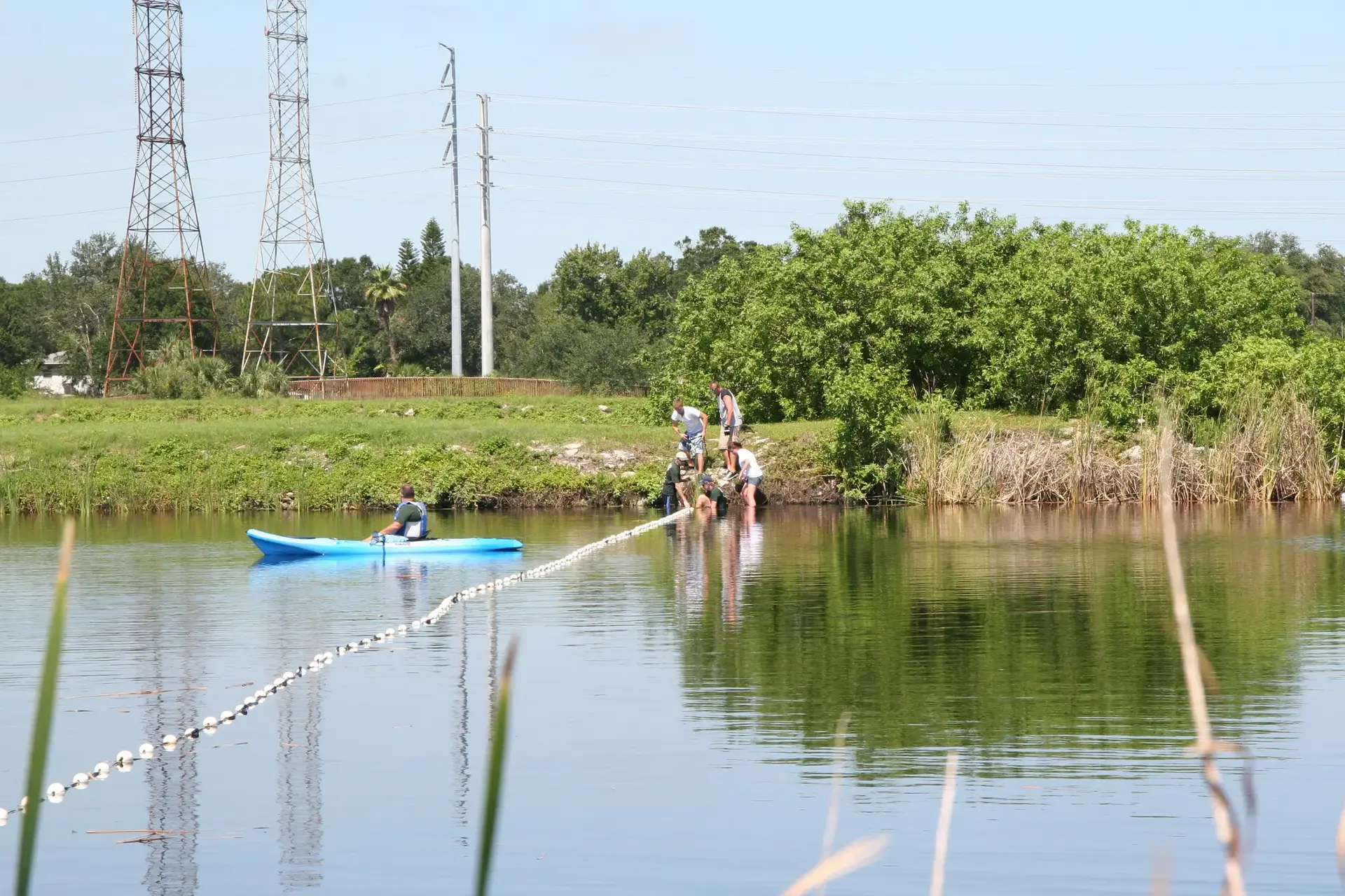 People pulling a chain across a river, one person in a blue kayak.