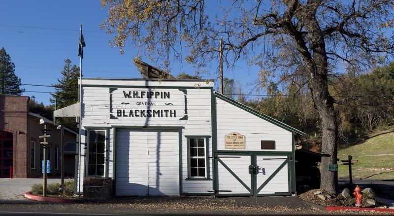 White historic blacksmith building under a clear sky, with a large bare tree.
