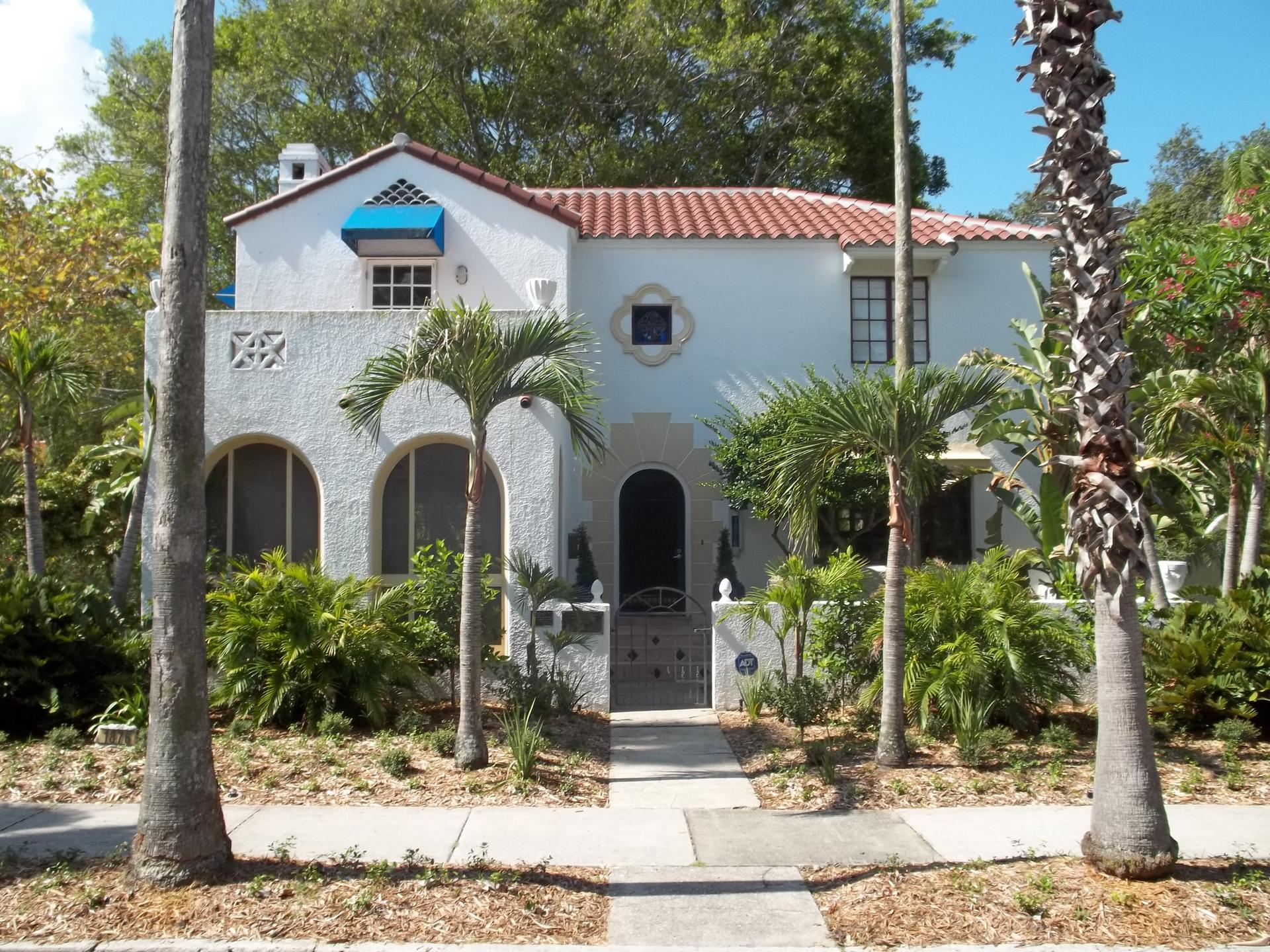 White house with red tile roof, surrounded by palm trees and lush greenery.