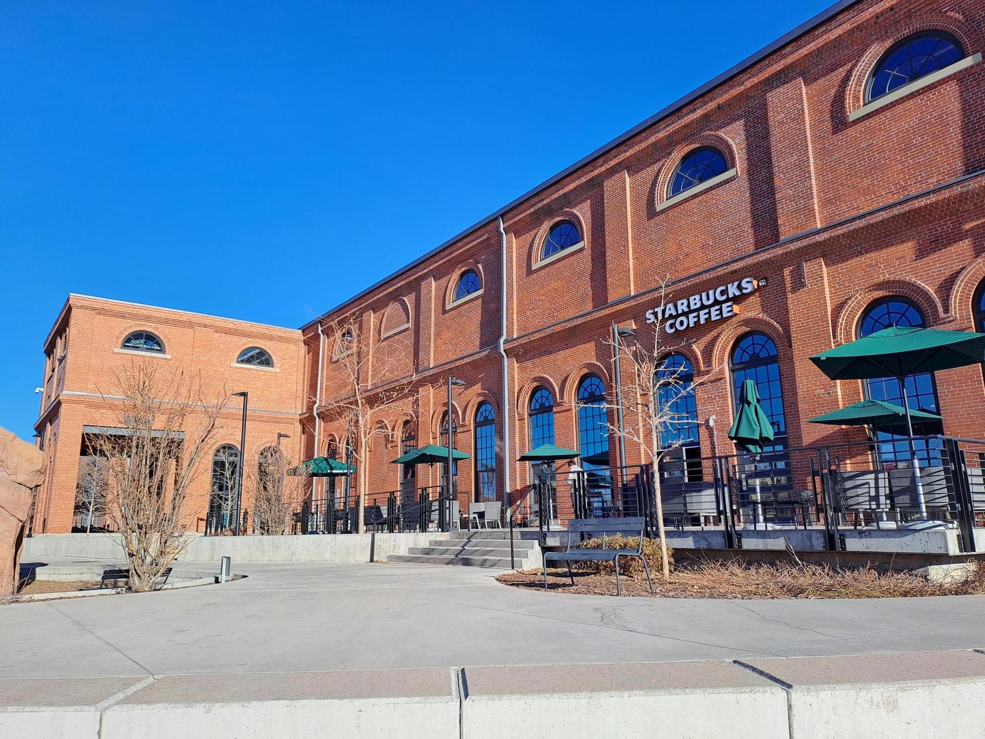 A large brick building with a patio and green umbrellas under a clear blue sky.