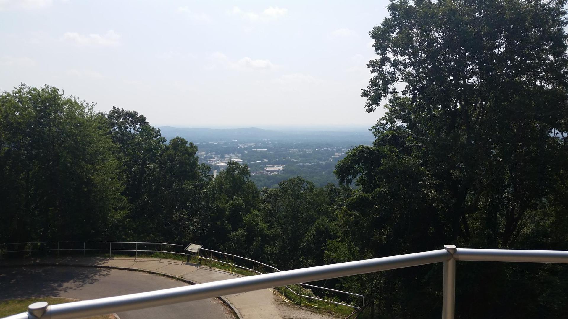 Overlook of a distant city through lush green trees on a bright day.