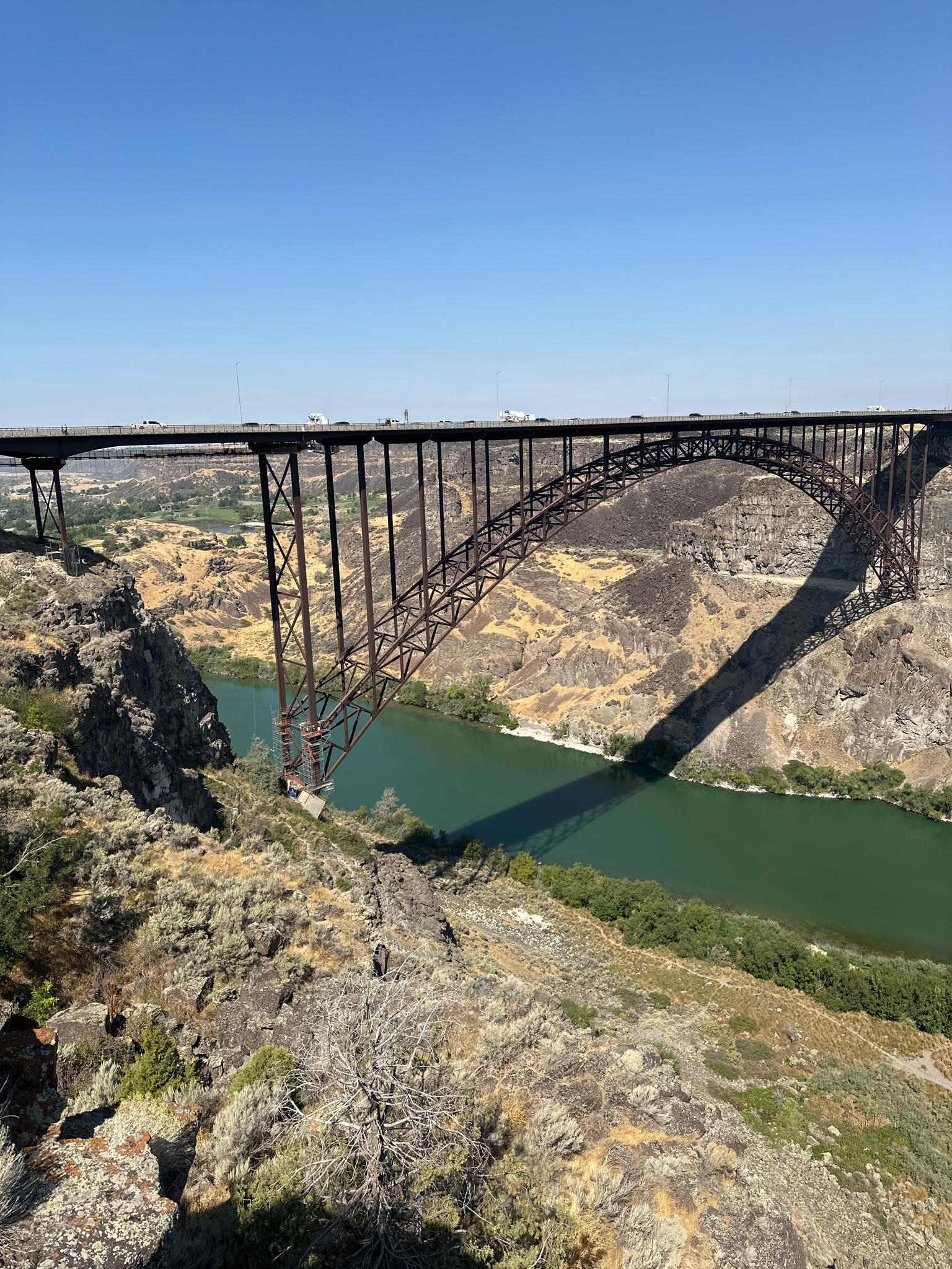 Sunny view of a large steel arch bridge casting a long shadow over a river.