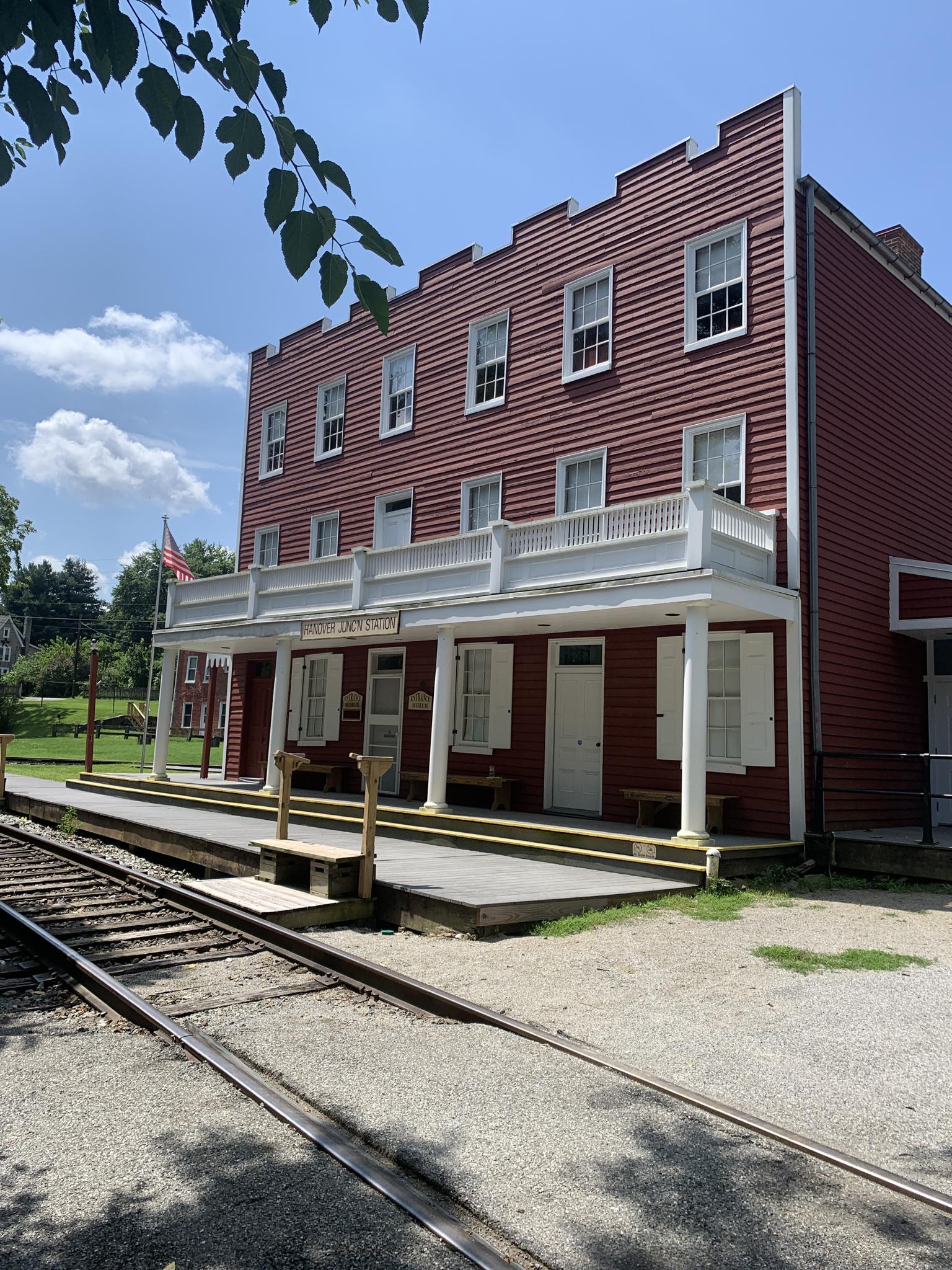 Historic red building with white trim next to train tracks on a sunny day.