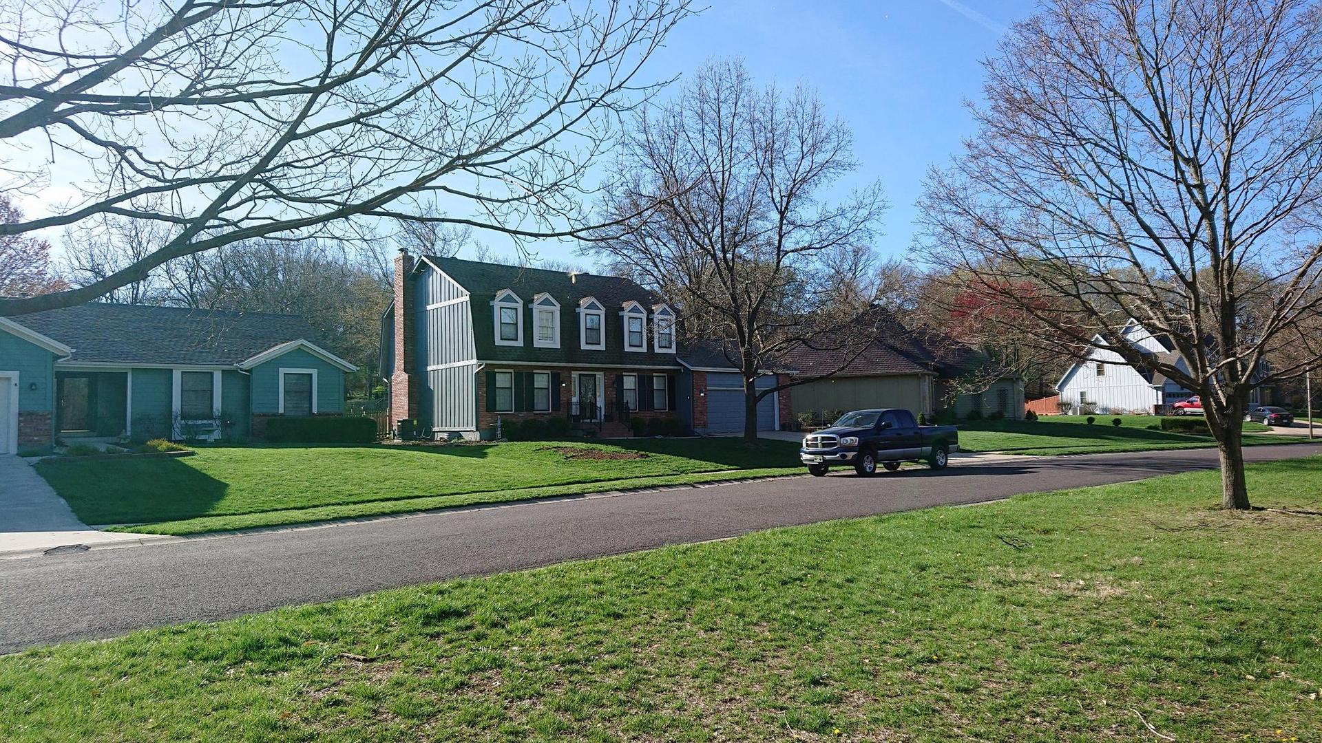 A suburban street with houses and green lawns under a clear sky.