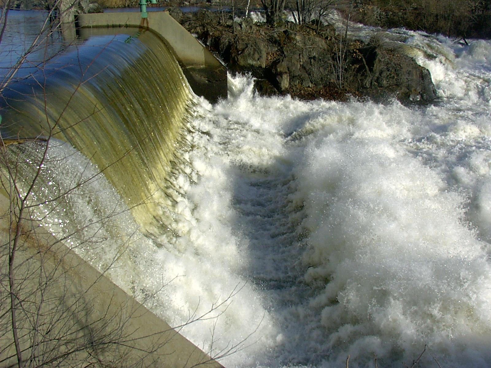 Water cascades over a concrete dam, creating foamy white rapids below.