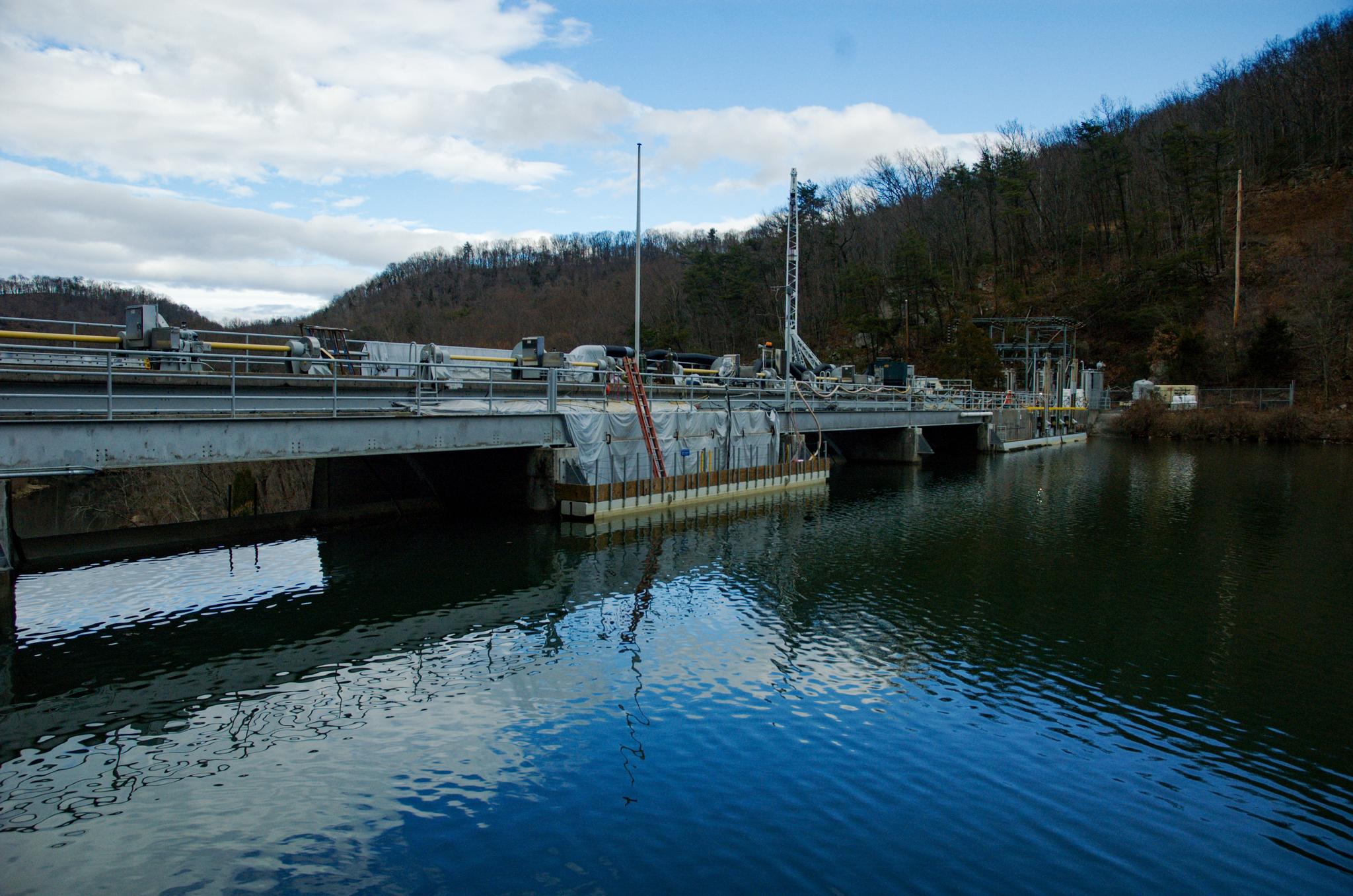 A large dam structure spans a wide river under a partly cloudy sky.