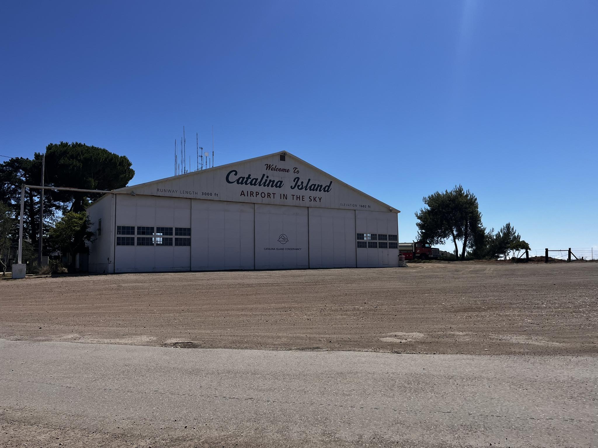 Large white hangar building with trees under a clear, bright blue sky.