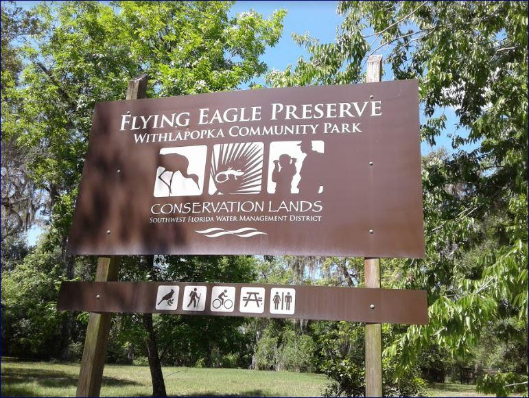 A large brown park sign with activity icons, surrounded by green trees.
