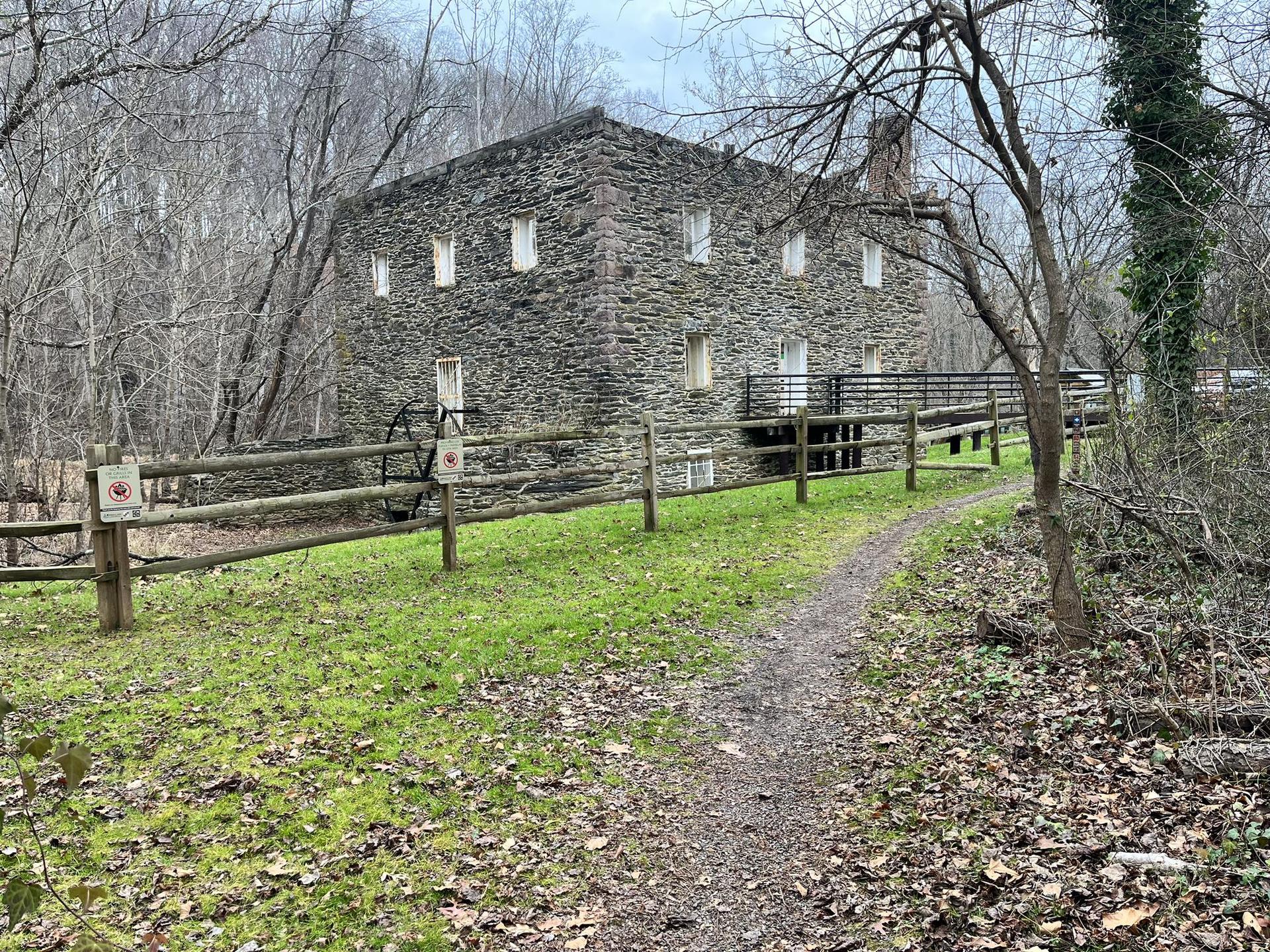 Overcast view of a stone building beside a dirt path and wooden fence.