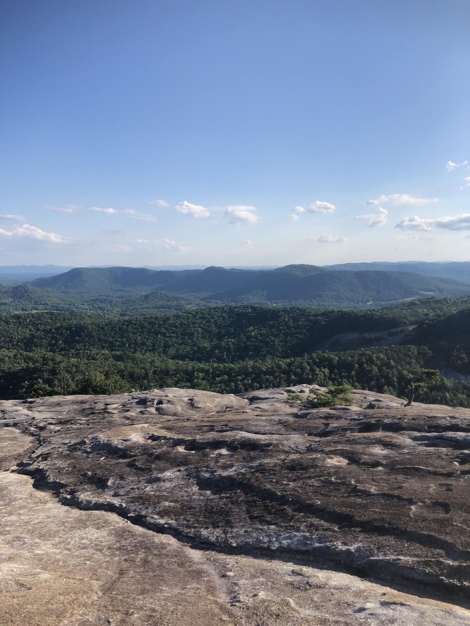 Rocky foreground overlooks distant forested mountains under a clear blue sky. - Stone Mountain Loop Trail