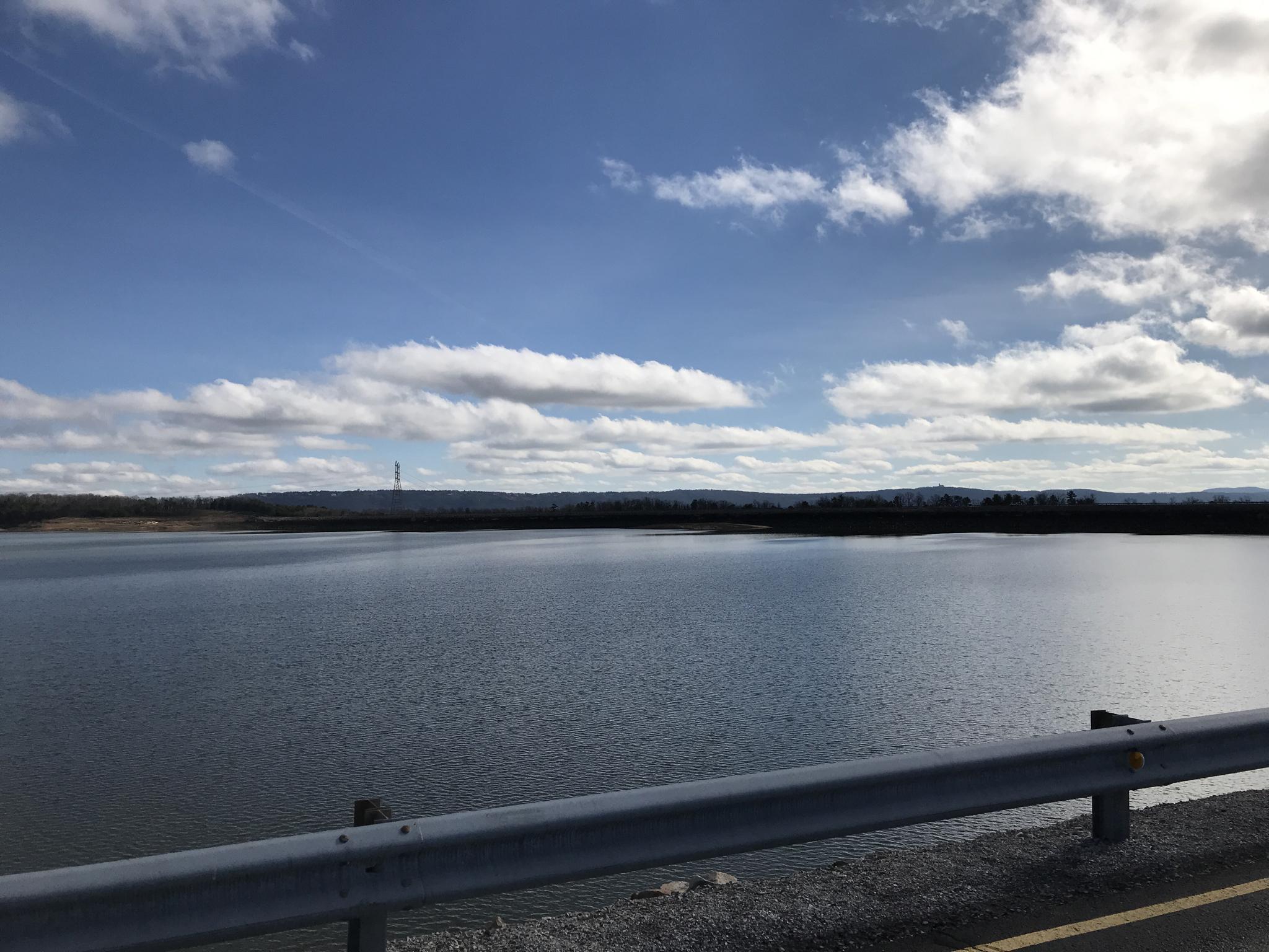 Vast lake under a partly cloudy sky, with a guardrail in the foreground.