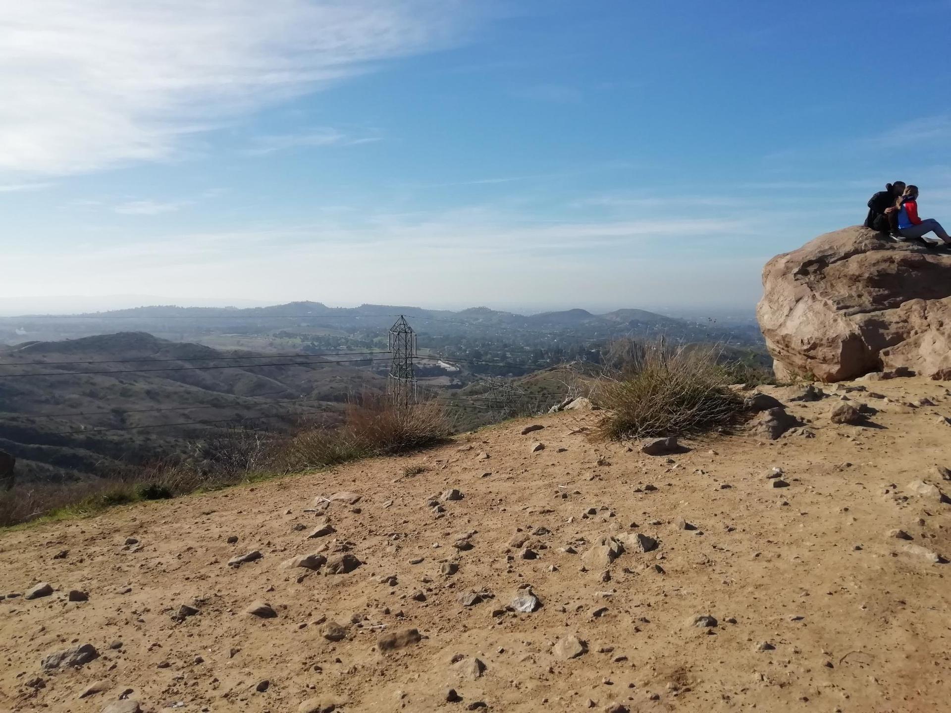 Two people sit on a large rock overlooking a vast, hazy landscape.