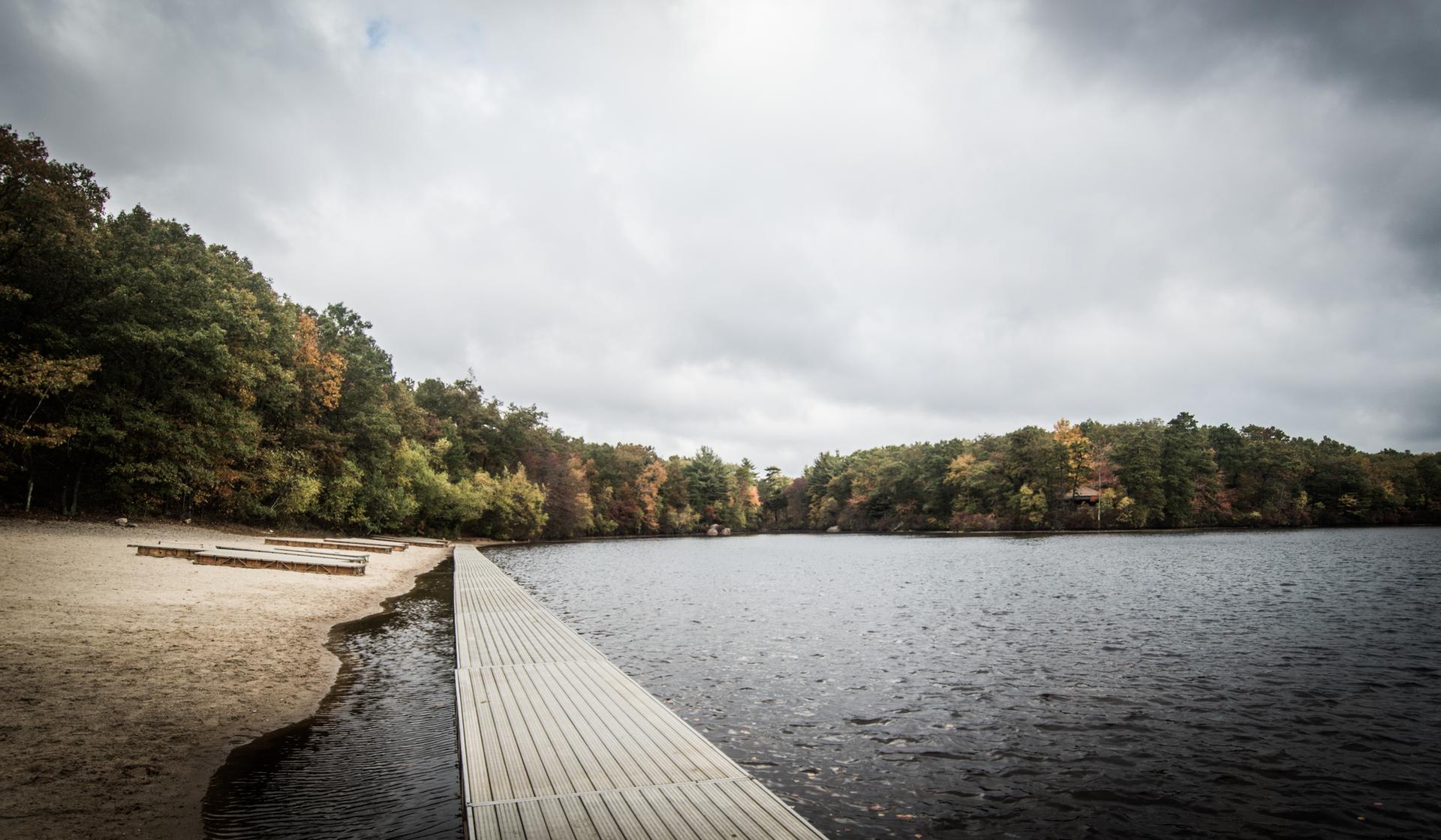 Long wooden dock extending into a lake, autumn trees, cloudy sky.