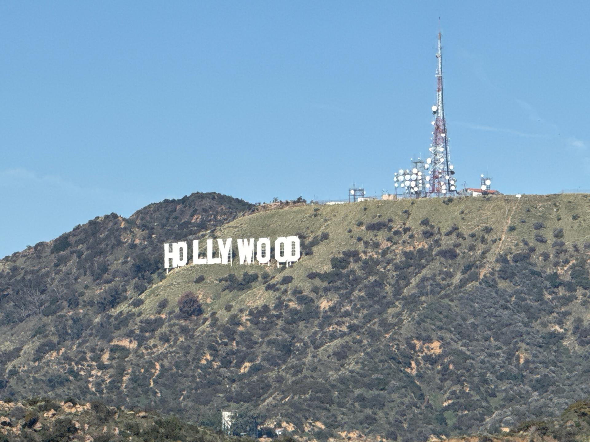 White letters on a dry, brushy hillside with a communication tower.