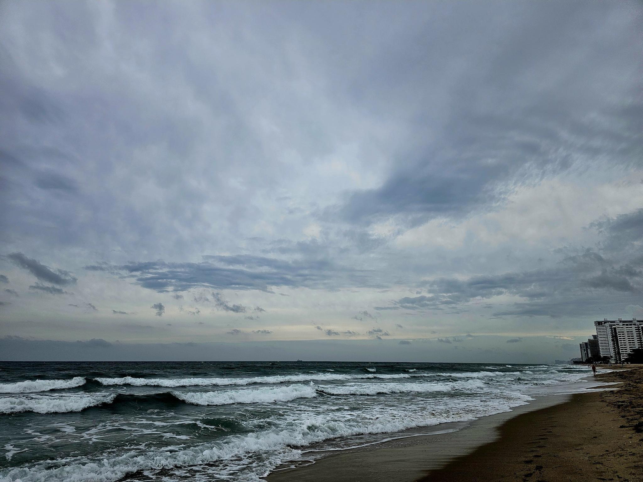 Ocean waves crash on a sandy beach under a dramatic cloudy sky.