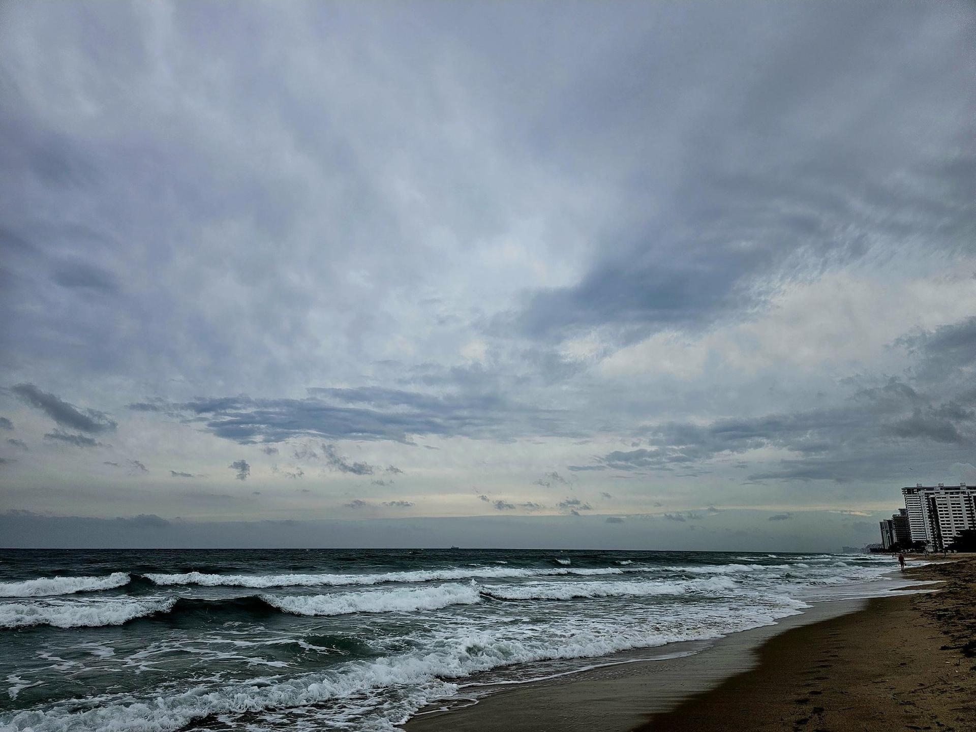 Ocean waves crash on a sandy beach under a dramatic cloudy sky.