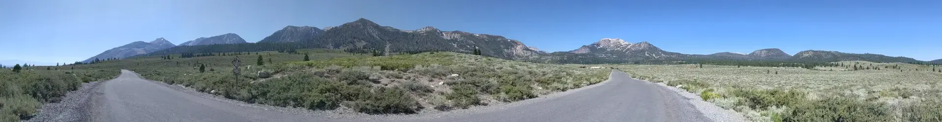 Panoramic view of a wide valley with a road, green fields, and mountains.