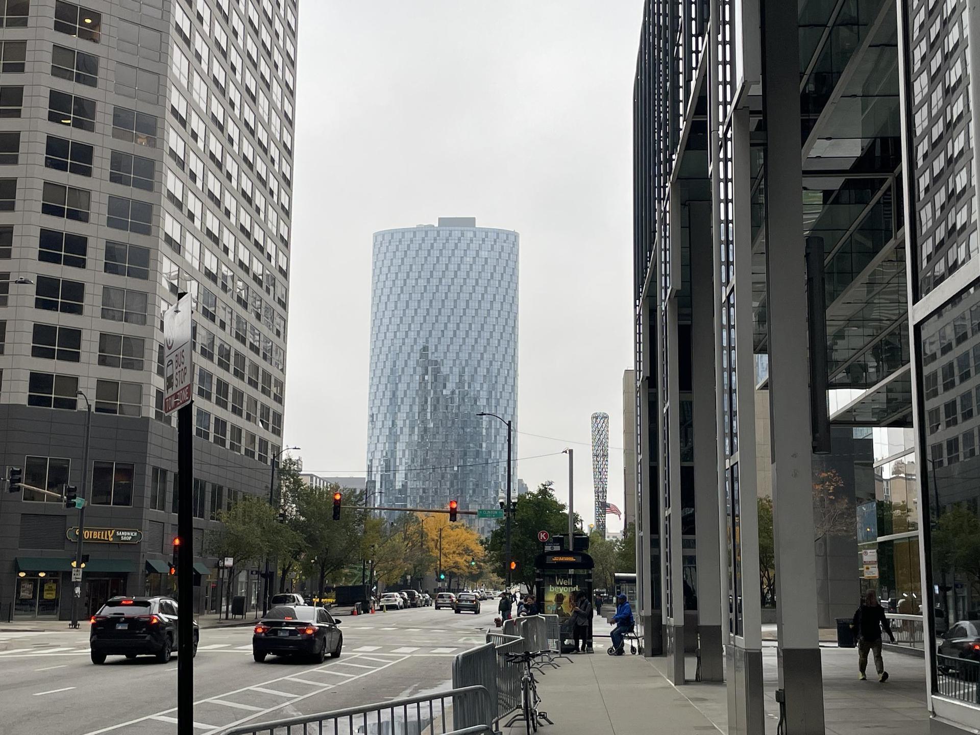 A city street with cars and pedestrians, flanked by modern skyscrapers.