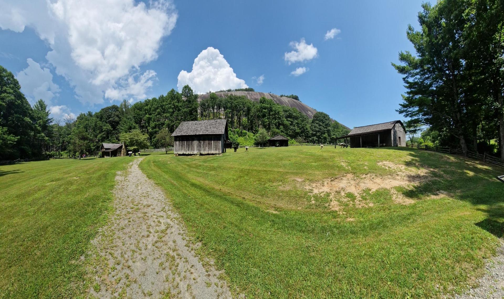 Grassy field with a dirt path, rustic buildings, and a large rock dome.