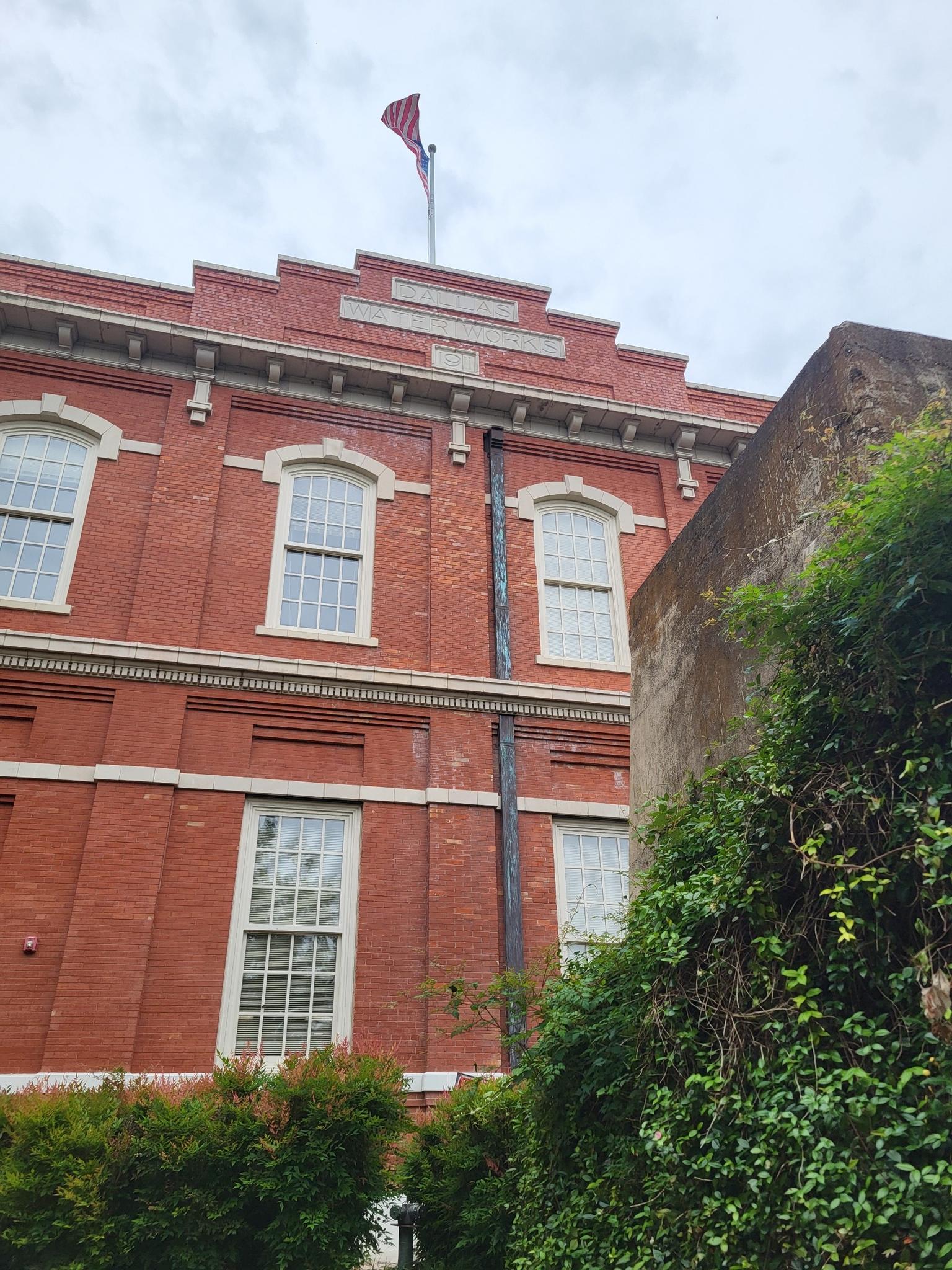 Tall red brick building with many windows, partially covered in green ivy.