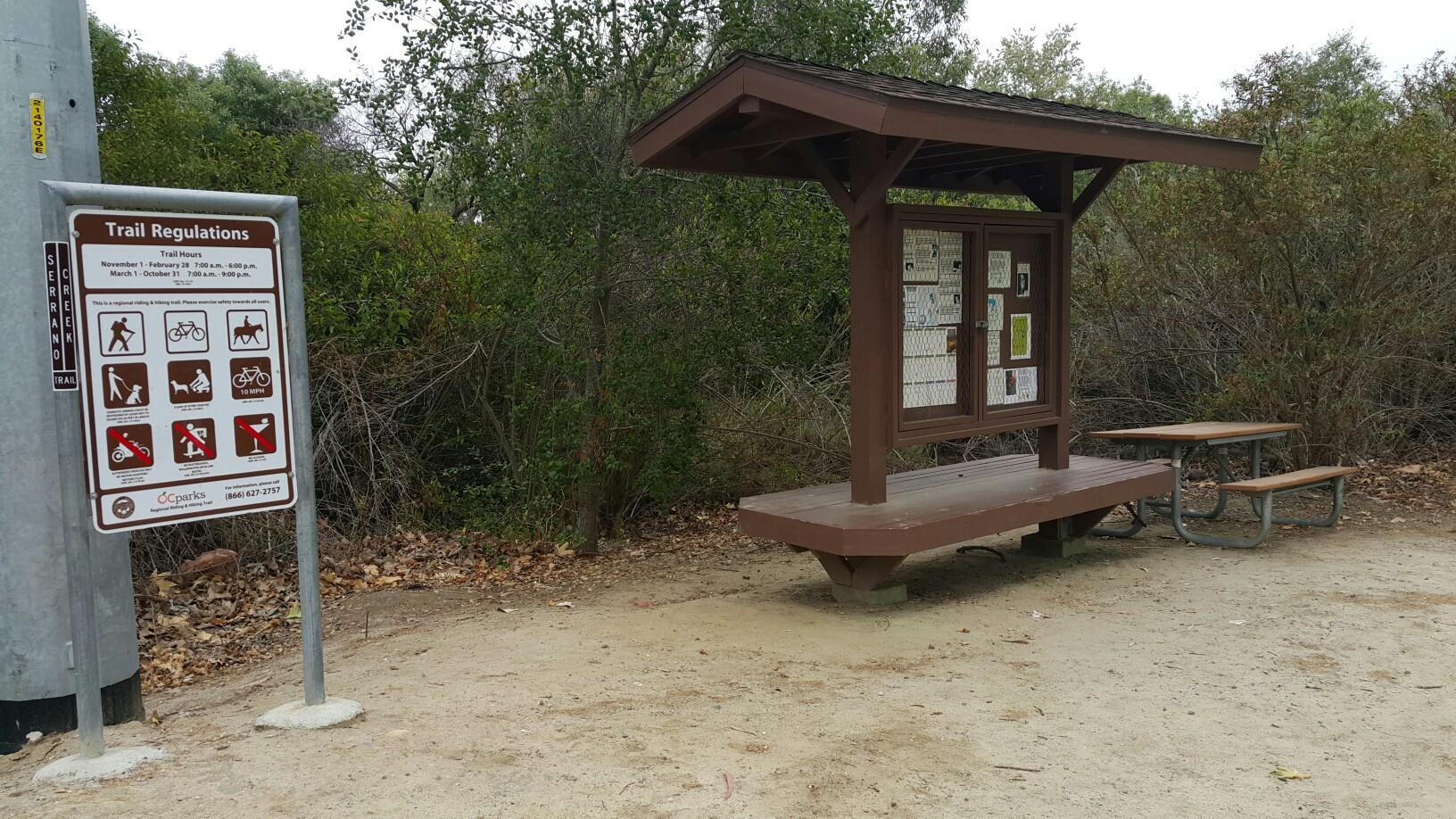 A trail regulations sign next to a covered bulletin board and picnic table.