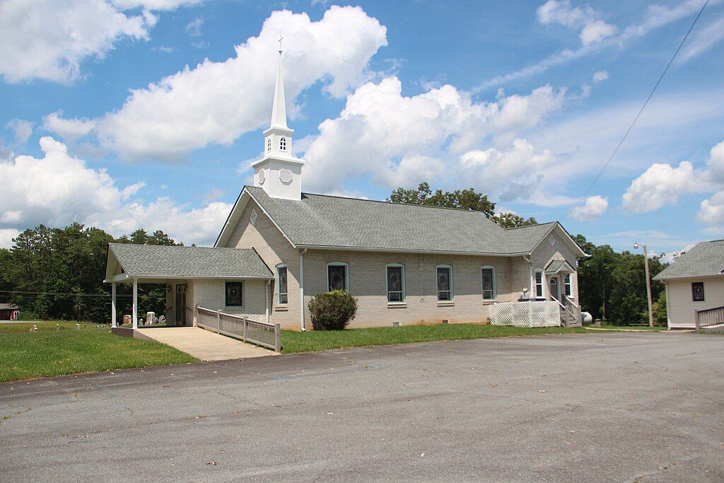 A white church with a steeple under a bright, cloudy sky. - Morgantown Hwy Climb from Hemp loop