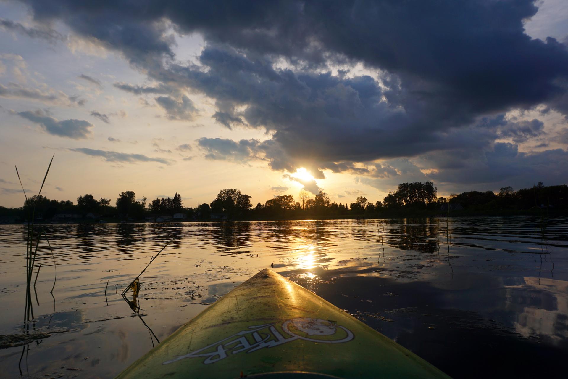 Kayak on calm water at sunset with dramatic clouds and golden light reflecting.