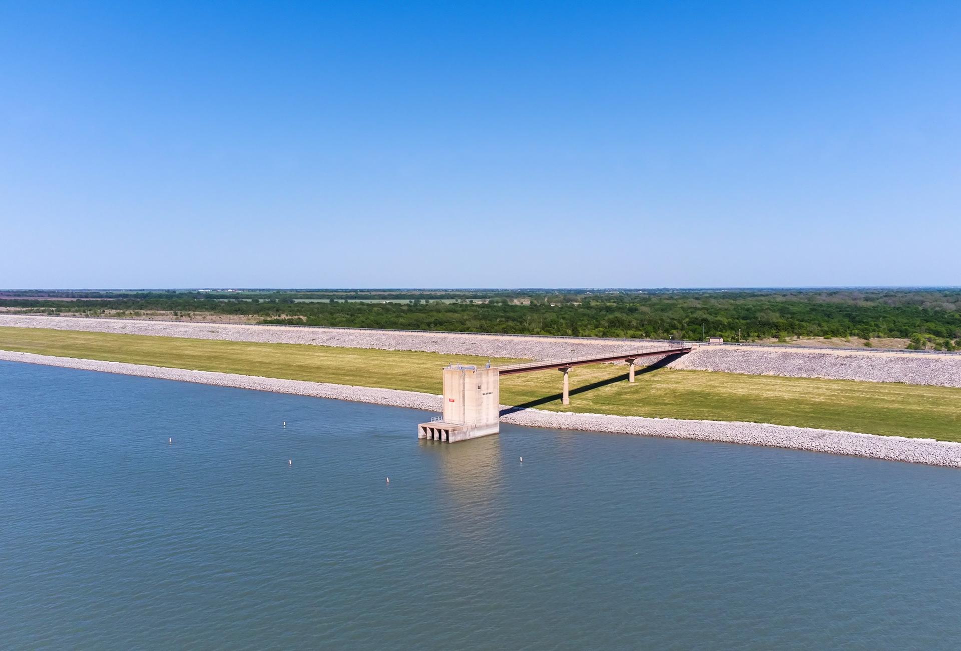 Vast reservoir under clear sky, with a concrete structure and walkway.