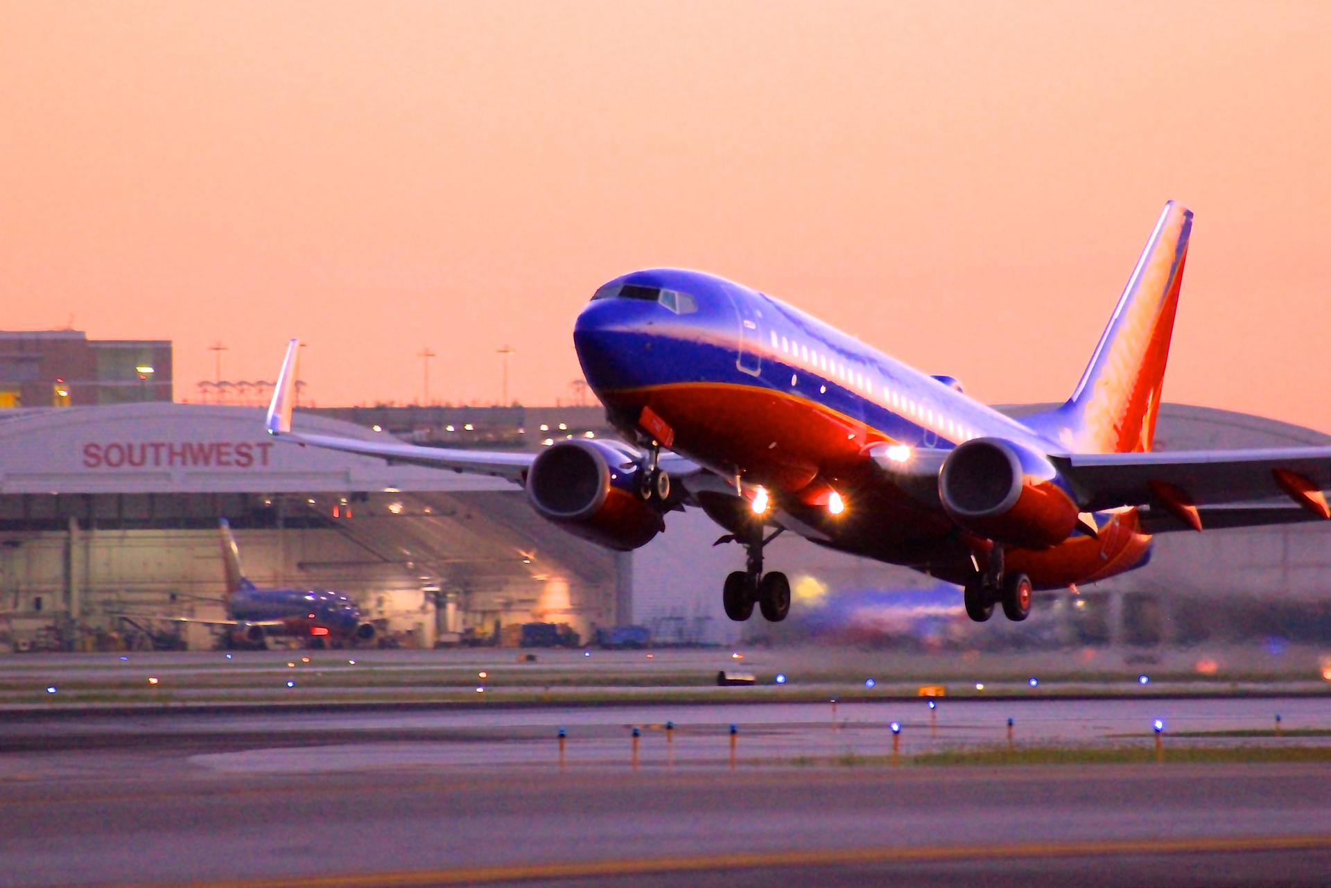 Blue and red airplane taking off from a runway at sunset.