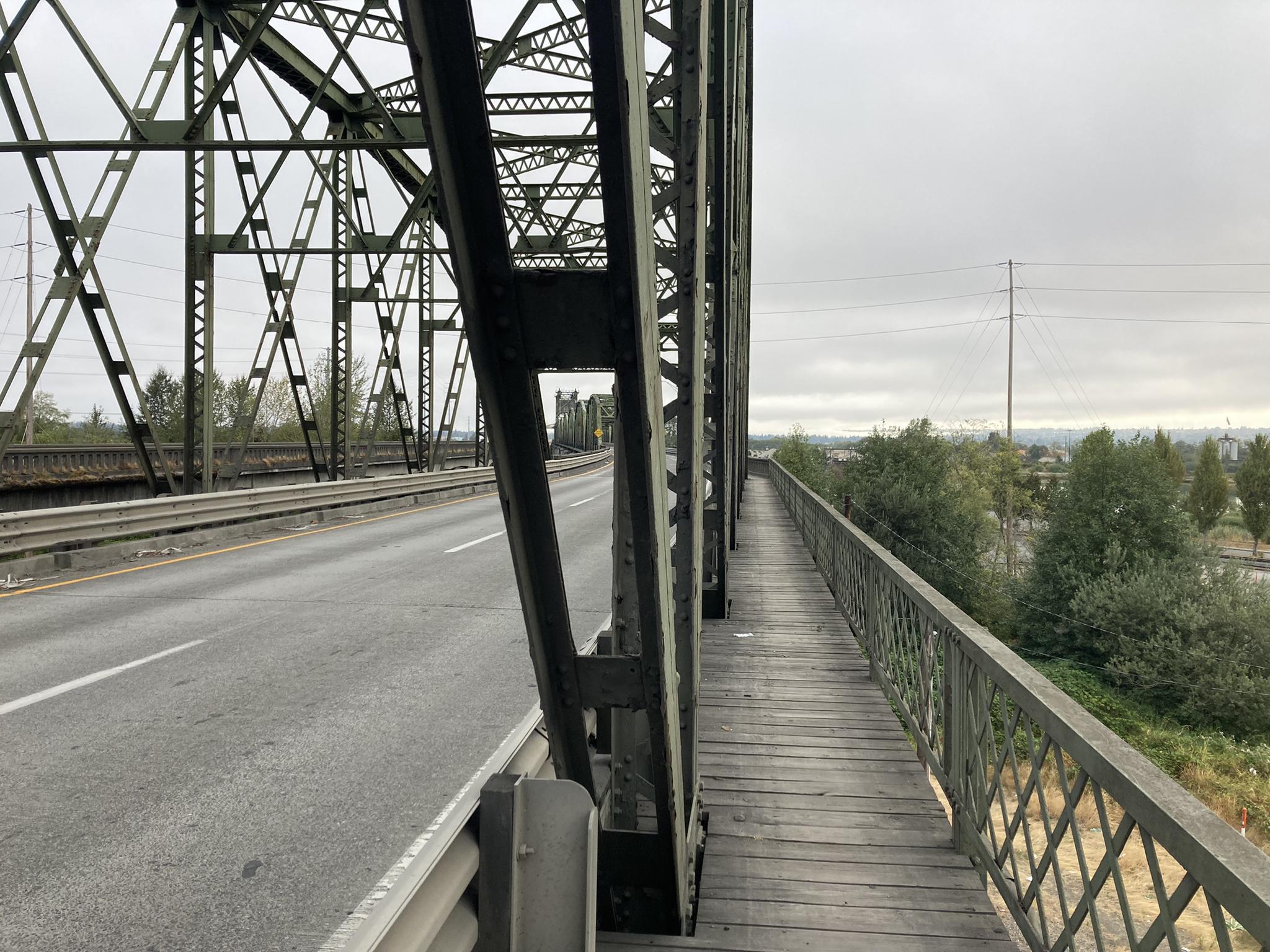 Side view of a metal bridge with a road and wooden pedestrian path.