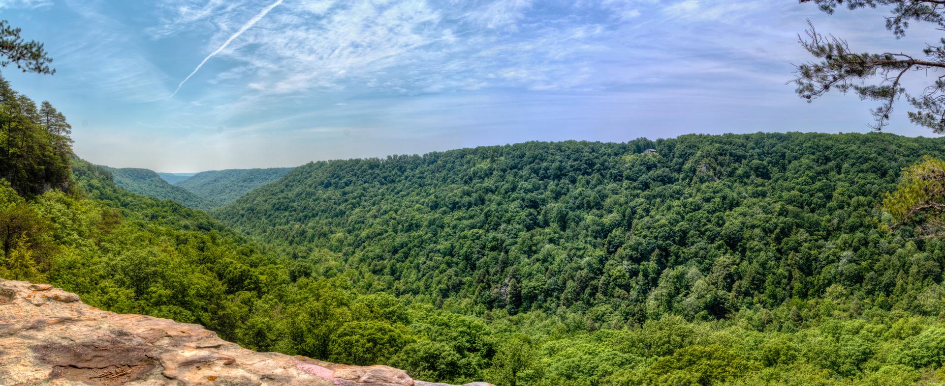 A panoramic view of a lush green valley under a bright, cloudy blue sky.
