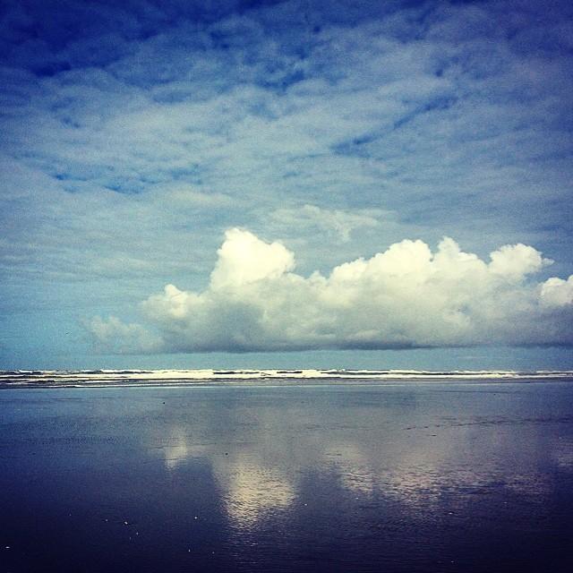 Expansive ocean reflects a cloudy sky with distant white waves.