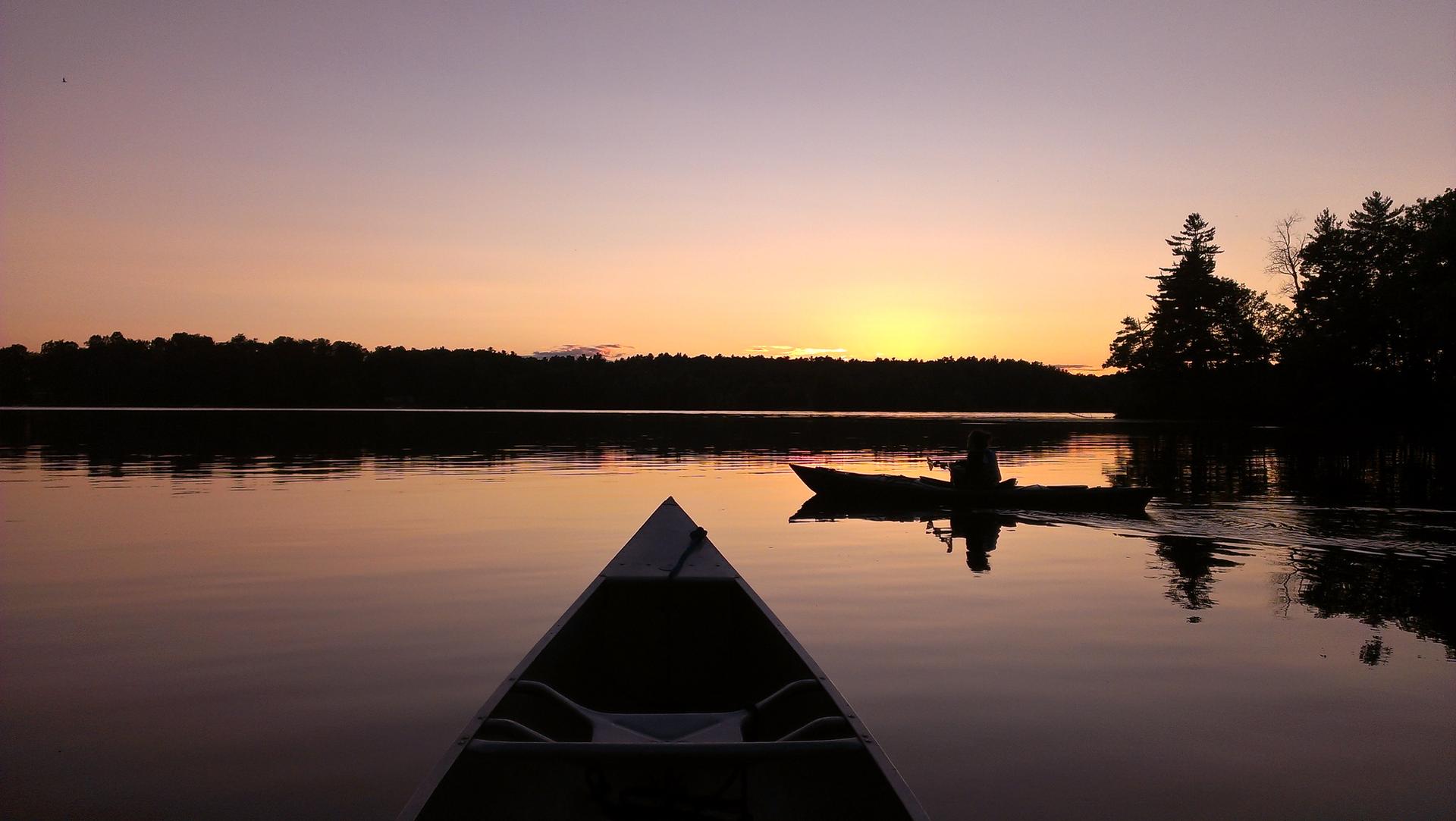 Silhouetted person paddling a boat on a calm lake at sunset.