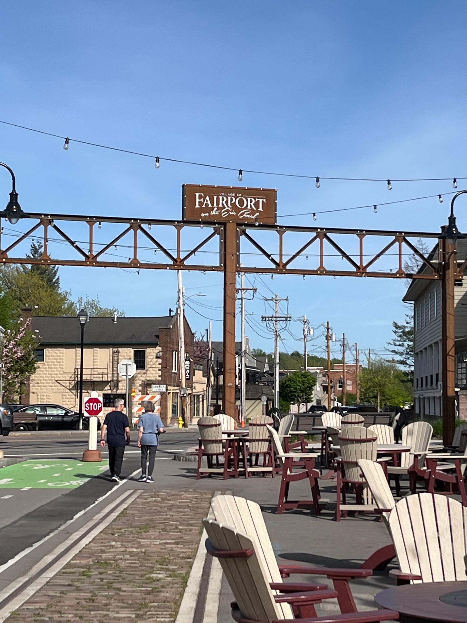 Outdoor dining area with two people walking under a sign, sunny.