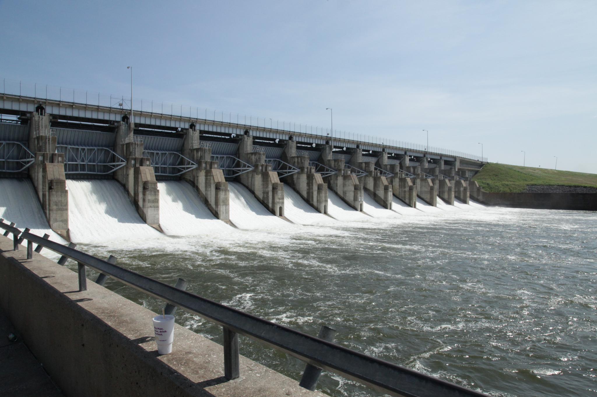 A large dam with water rushing through multiple gates on a sunny day.