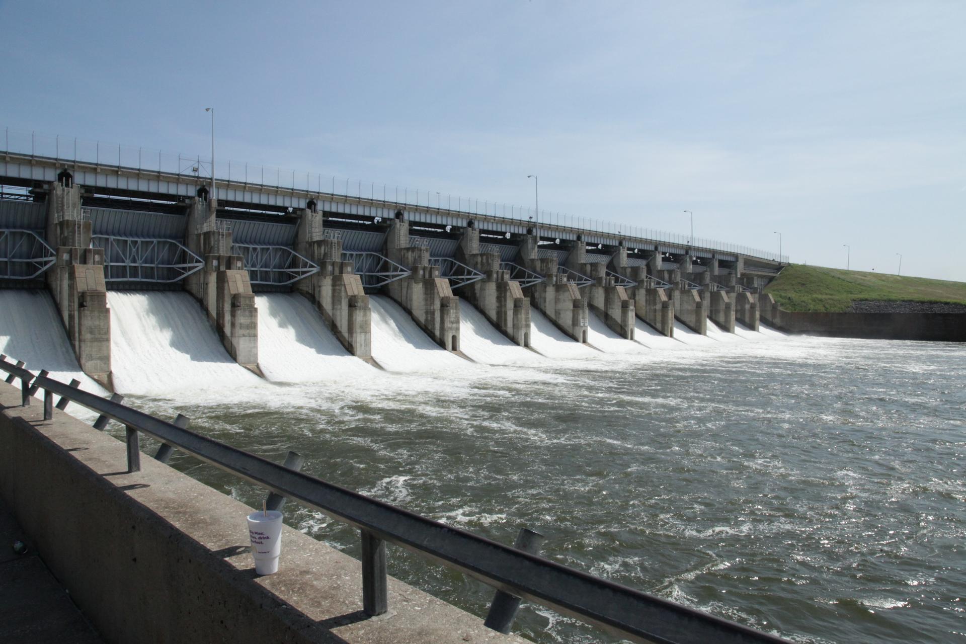 A large dam with water rushing through multiple gates on a sunny day.