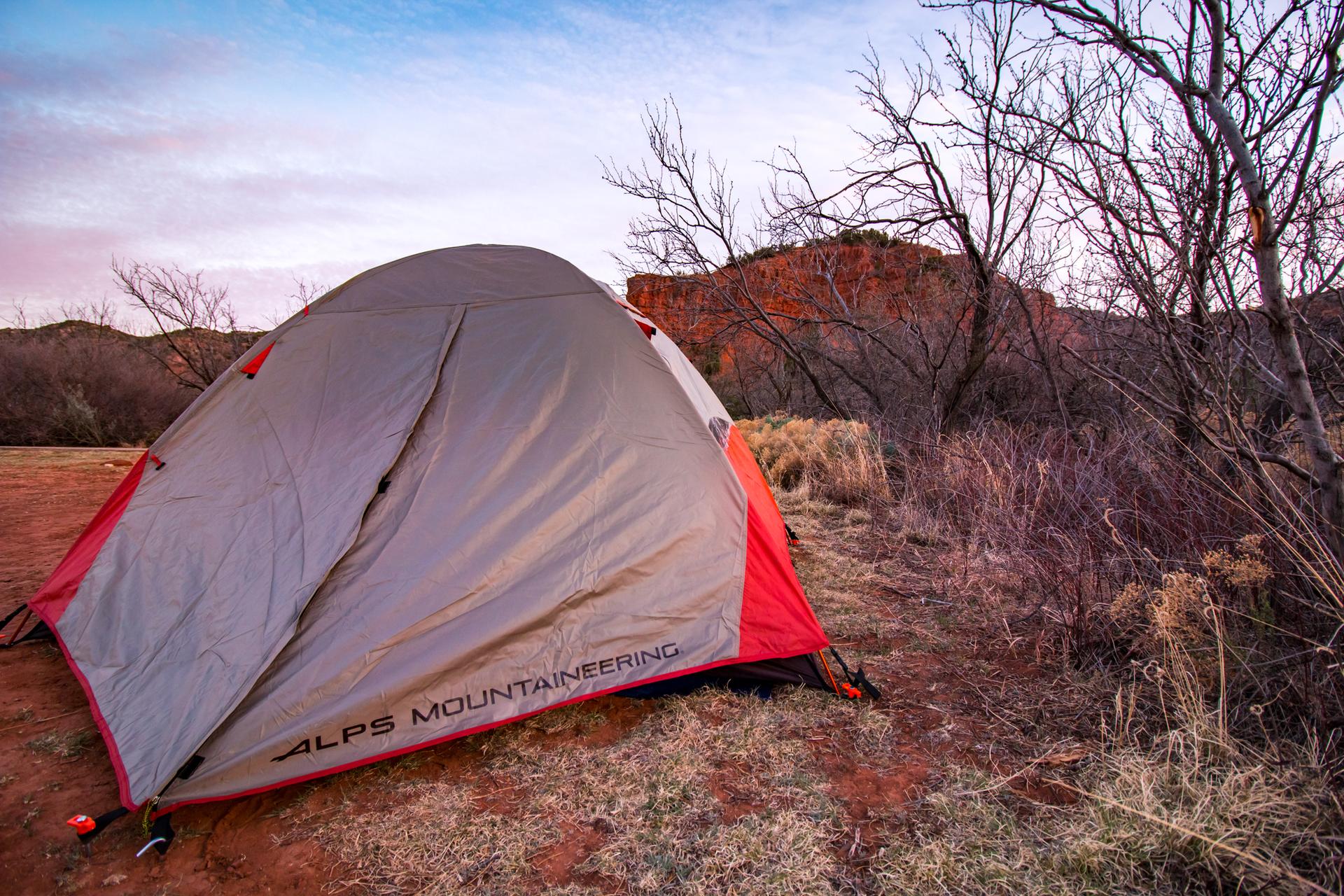 A gray and red tent pitched in a desert landscape at sunrise.