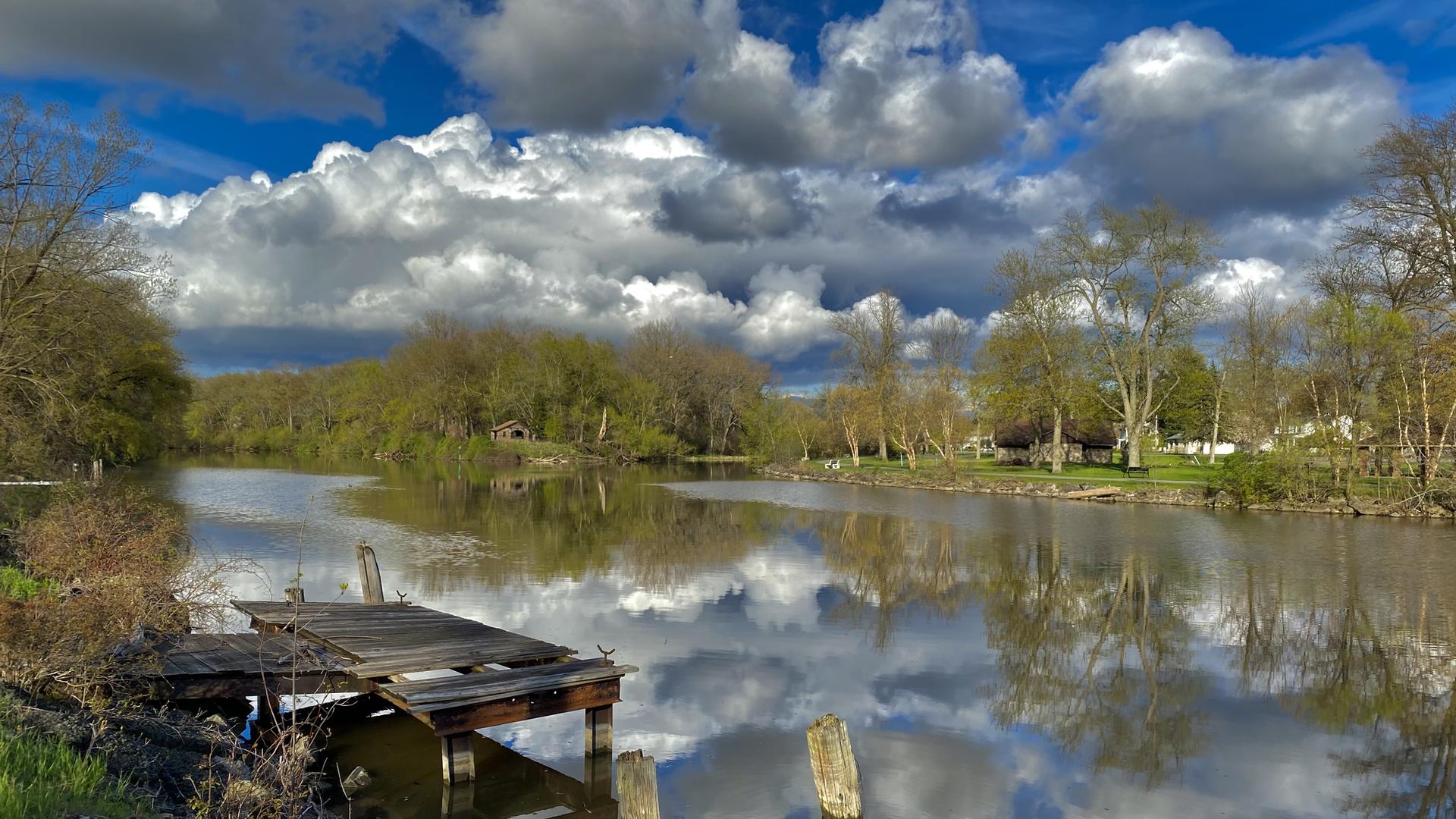 A wide river with an old wooden dock, reflecting dramatic clouds and trees.