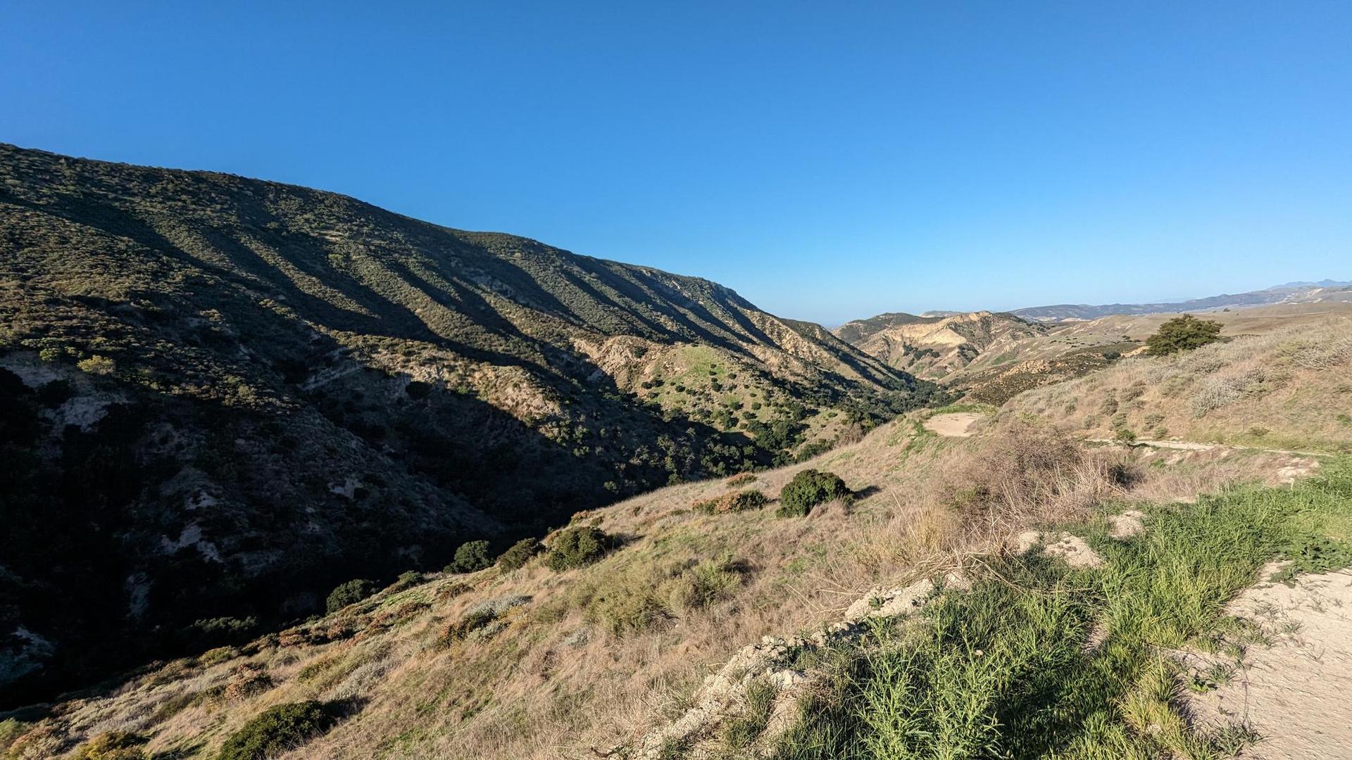 Steep, sunlit hillsides and a valley under a clear blue sky.